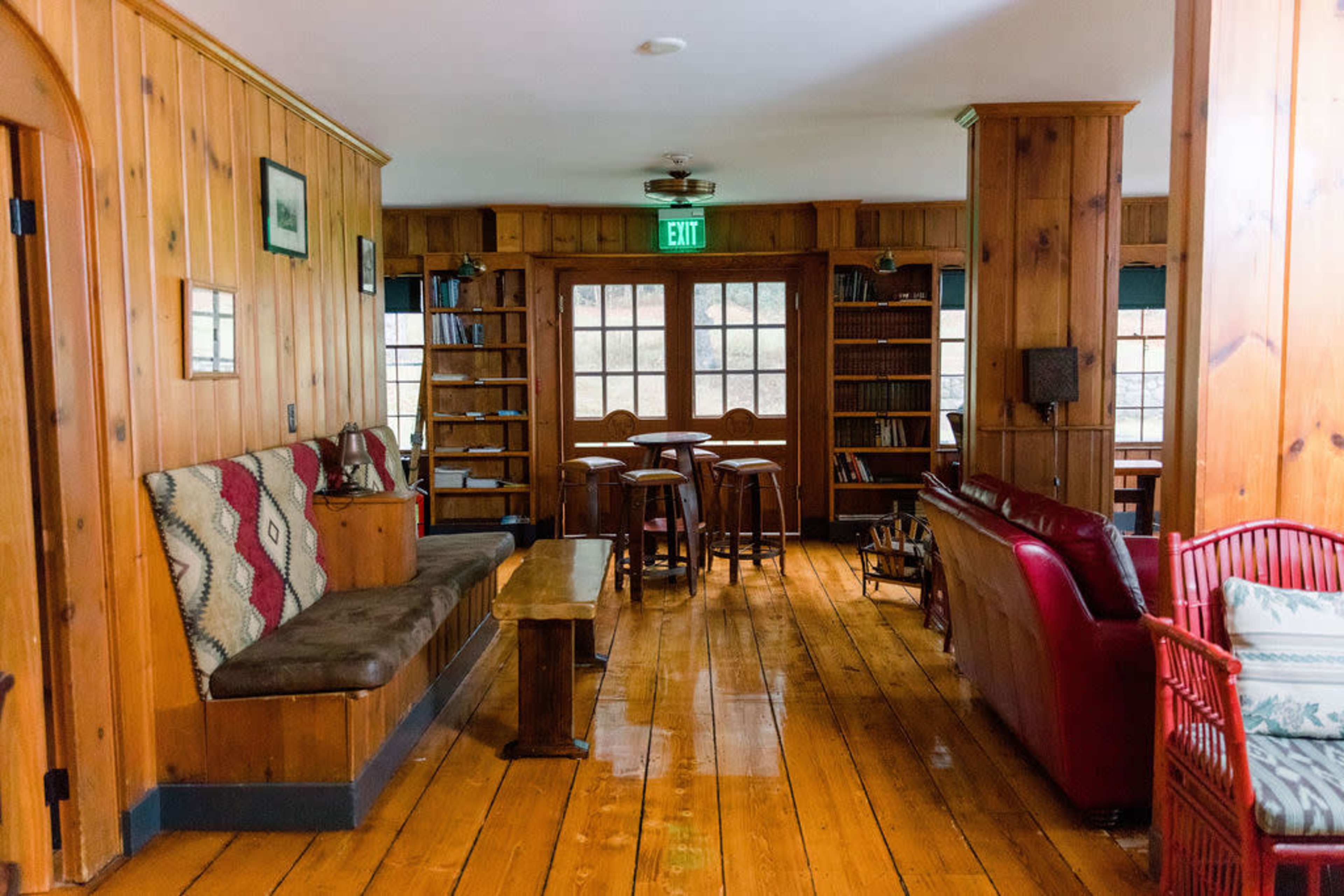 A timber-paneled room with a seating area, a wooden table and stools, bookshelves, and a red couch.