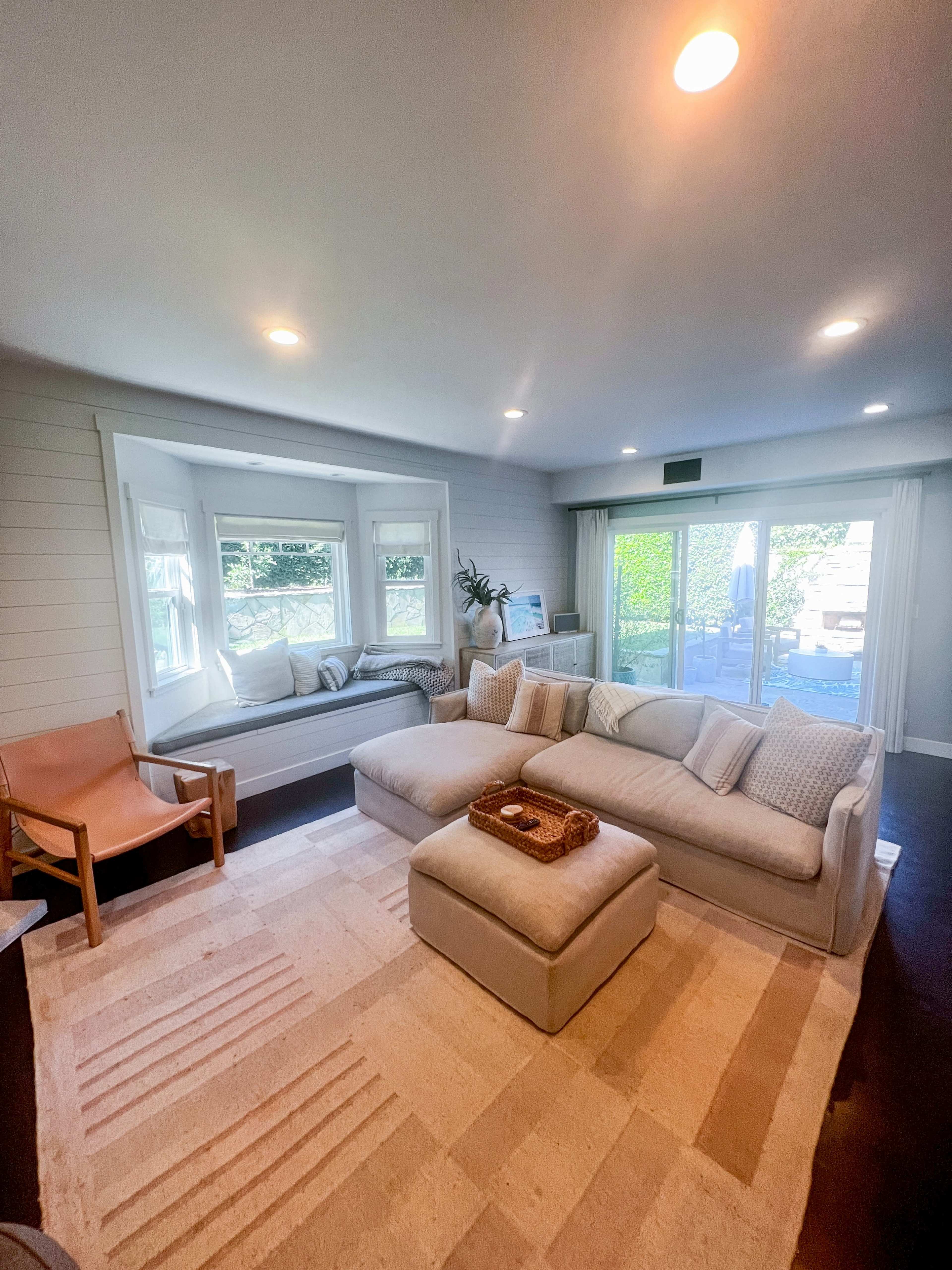 The living room features a sectional sofa, a leather chair, and a large area rug, with a view of the outdoor space through sliding glass doors.