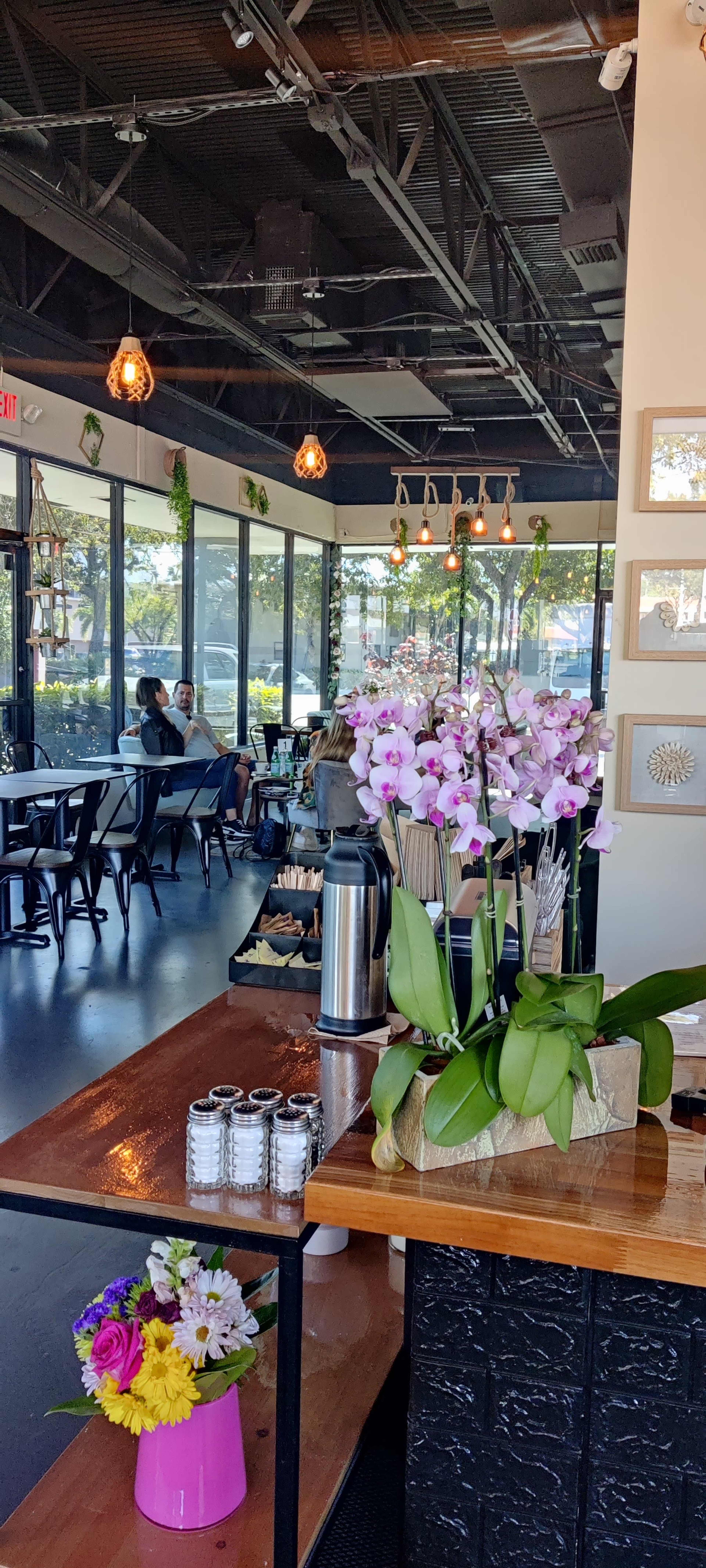 The interior of a café with seating arrangements, decorative plants, and a floral centerpiece on the counter.