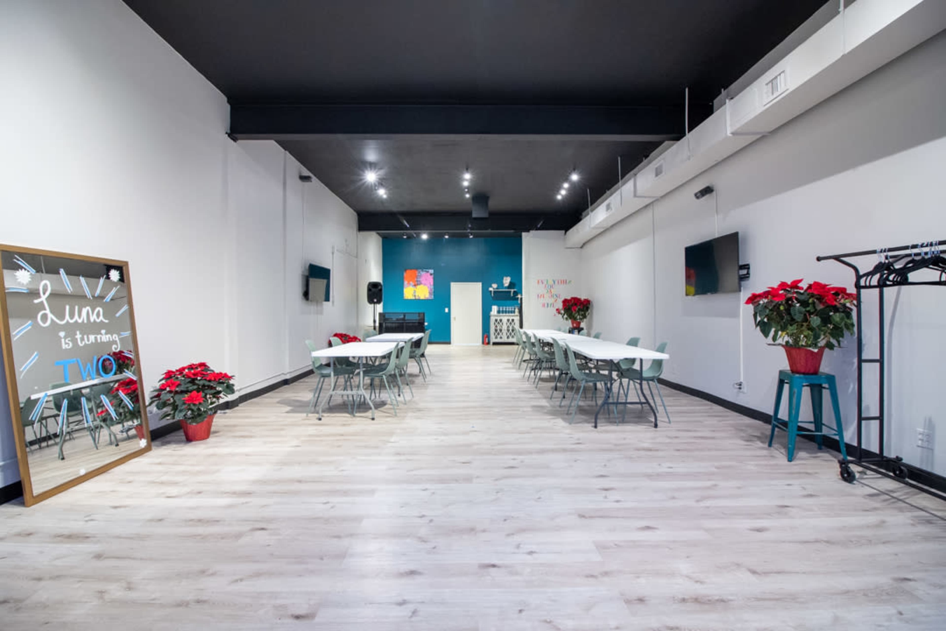 A spacious event room with multiple tables, chairs, a mirror on one wall, and red poinsettias arranged decoratively.