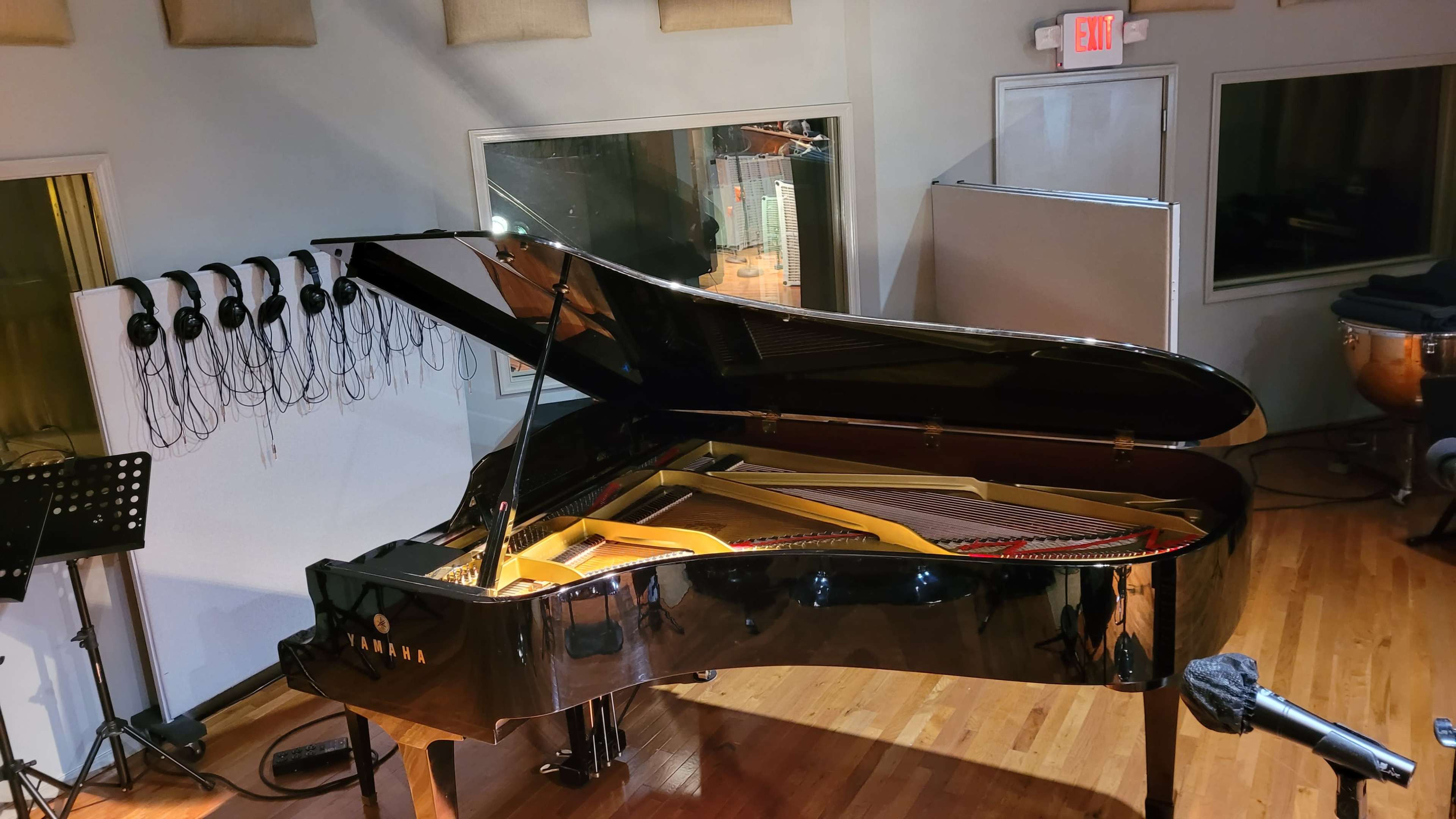 A Yamaha grand piano is positioned in a music studio with headphones hanging on the wall and a microphone set up nearby.