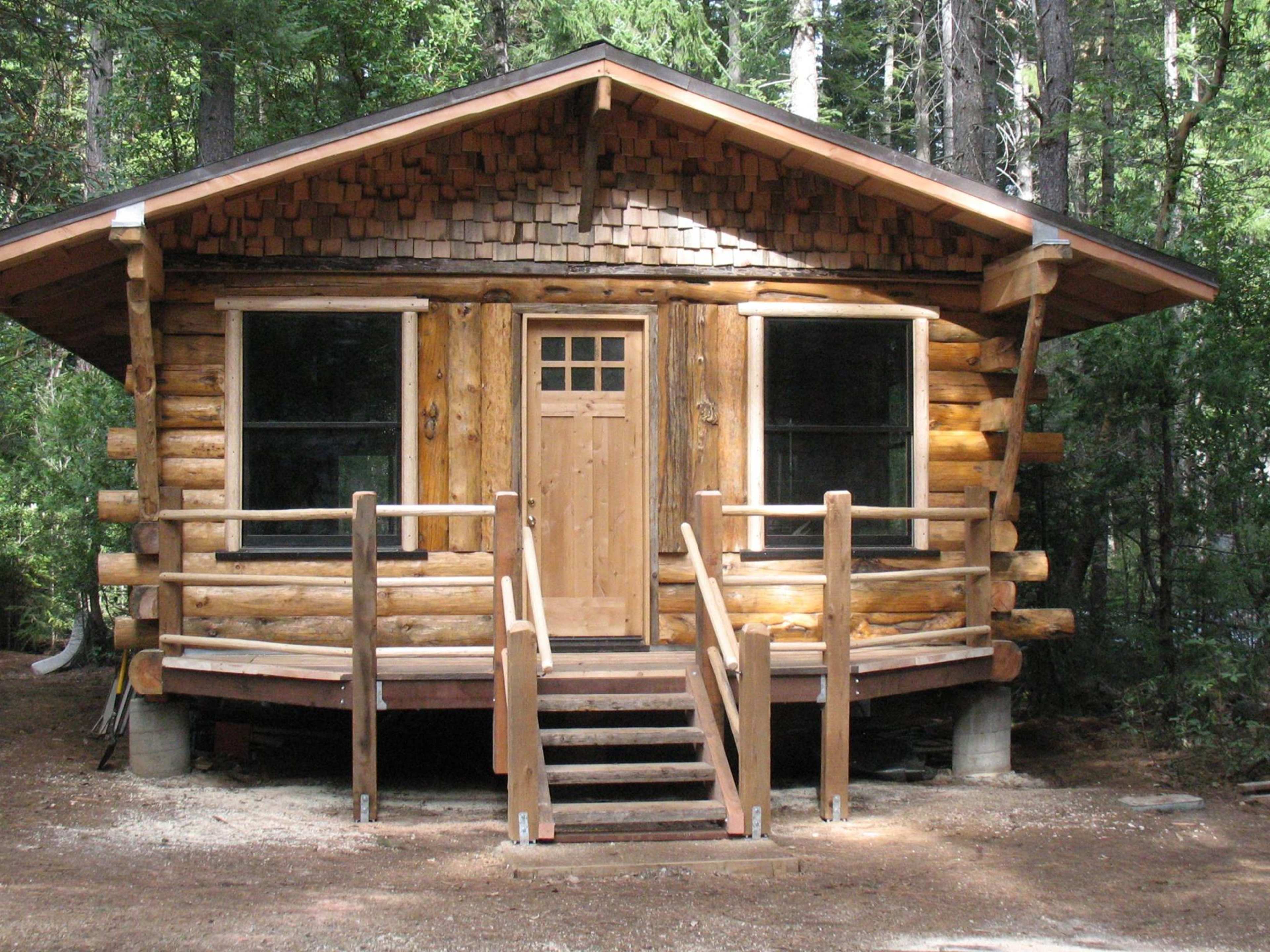 A wooden log cabin with a front porch and steps, surrounded by trees.