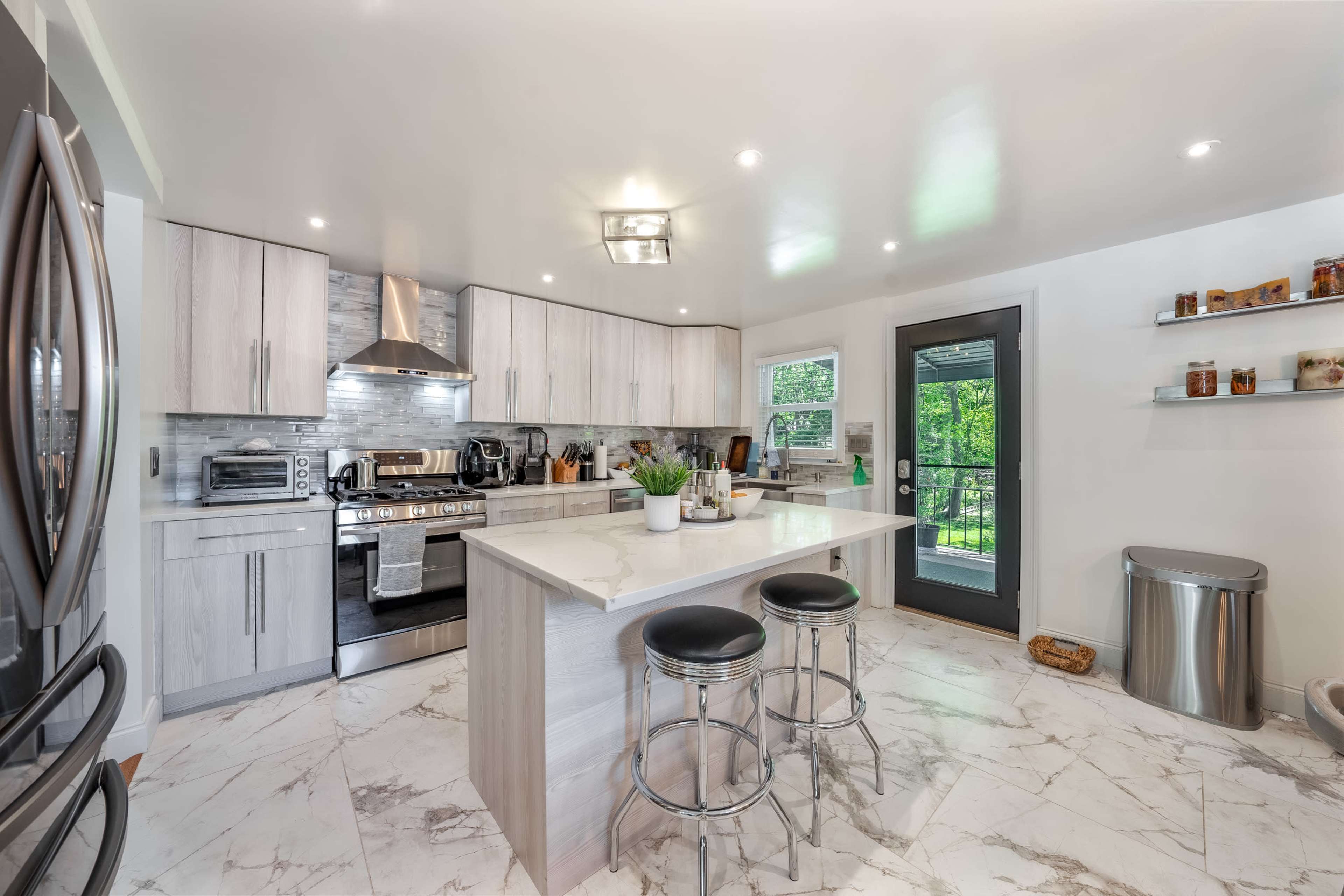A modern kitchen featuring a marble floor, stainless steel appliances, and a central island with bar stools.