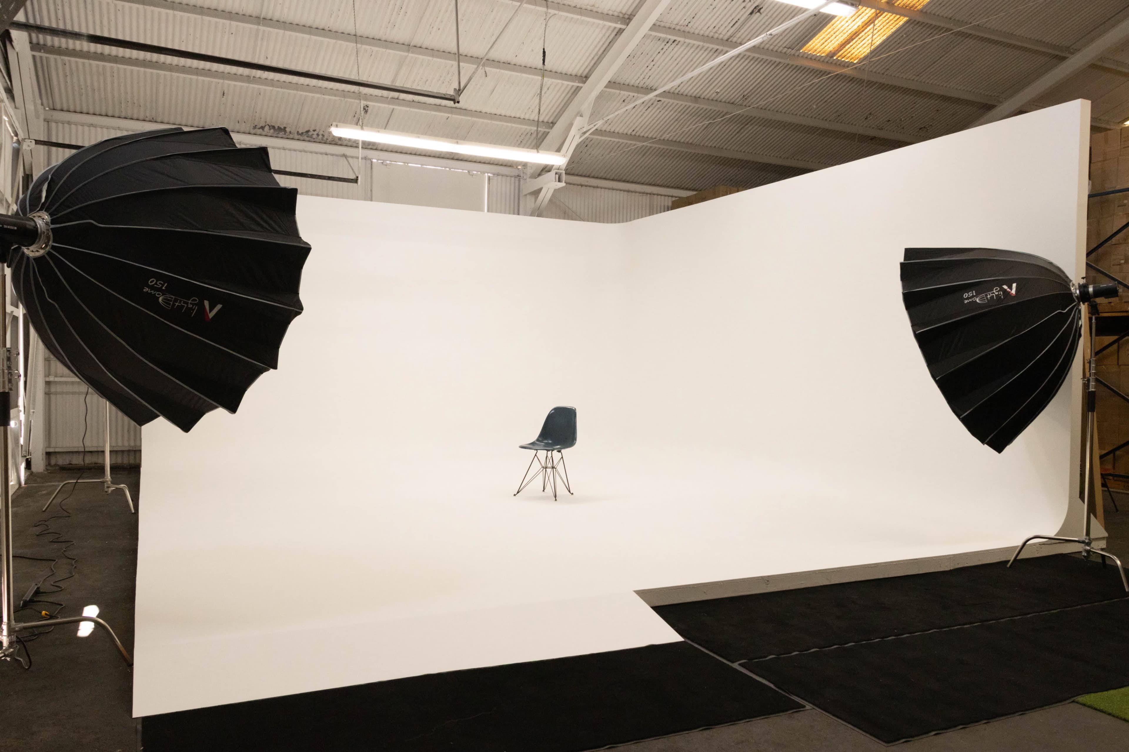 A single blue chair is positioned in the center of a photography studio with large softbox lights on either side.