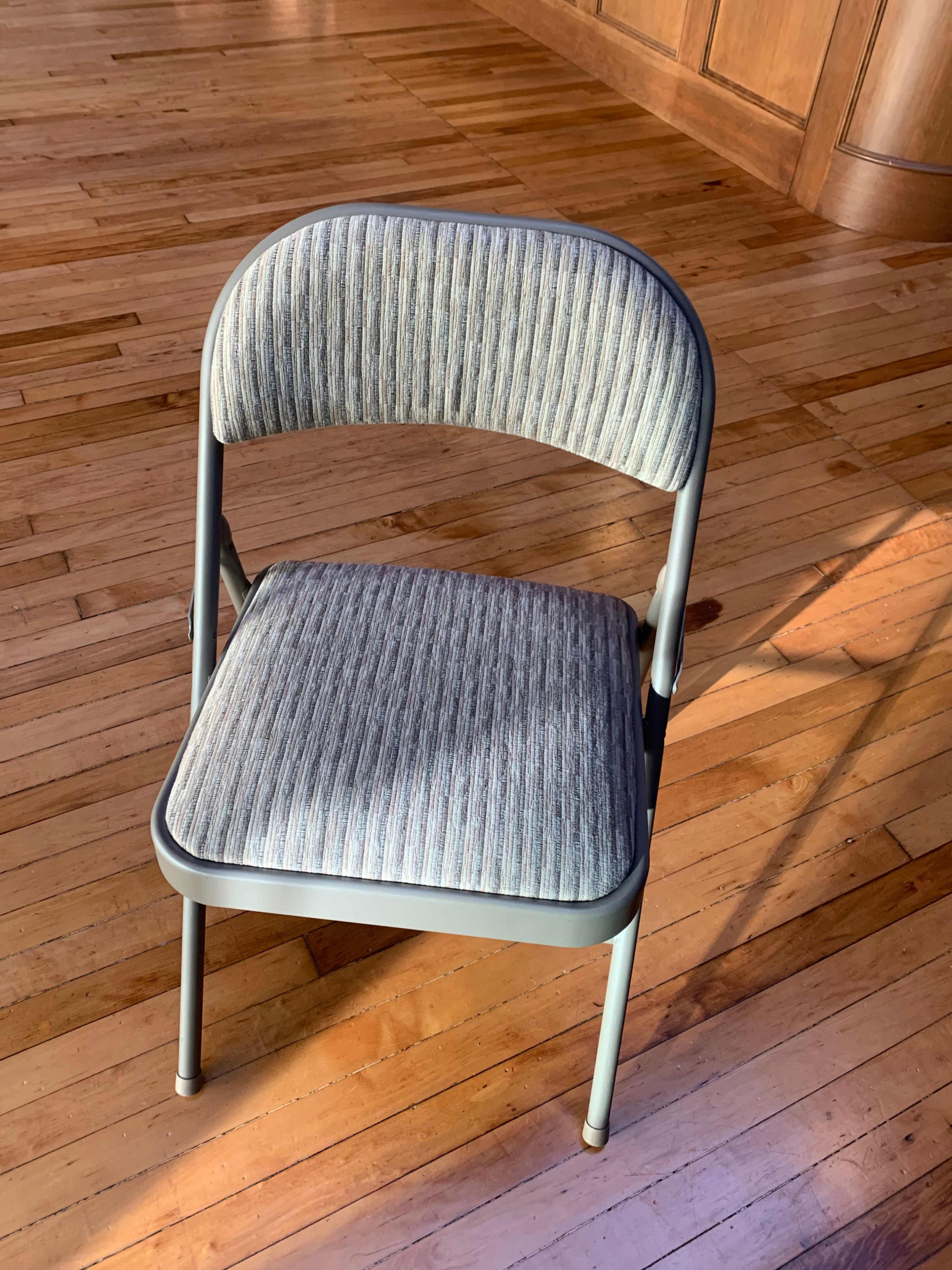 A metal folding chair with a striped fabric cover is positioned on a wooden floor.