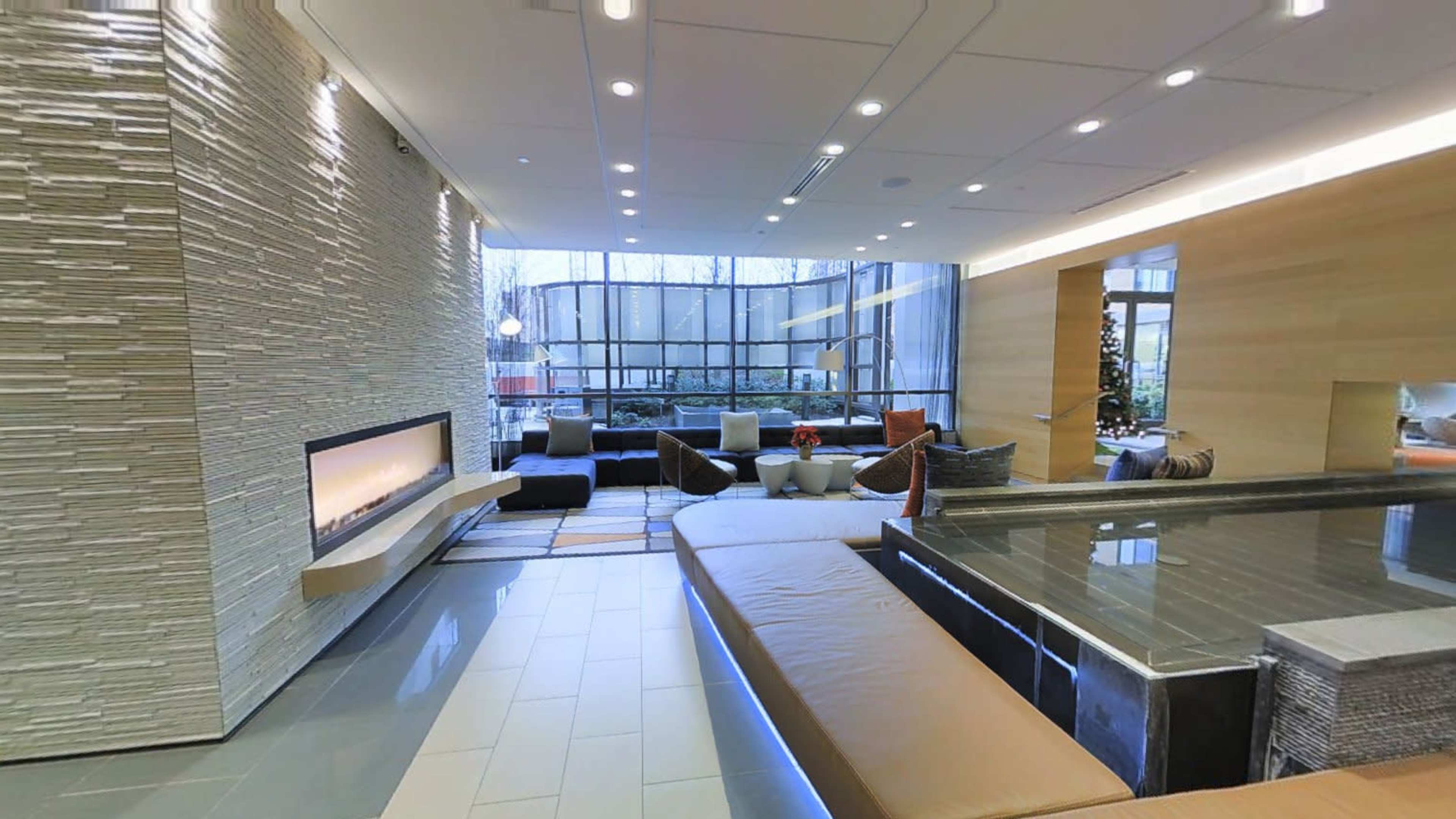 A modern lounge area with a fireplace, large windows, and a mix of seating options arranged around a stone platform.