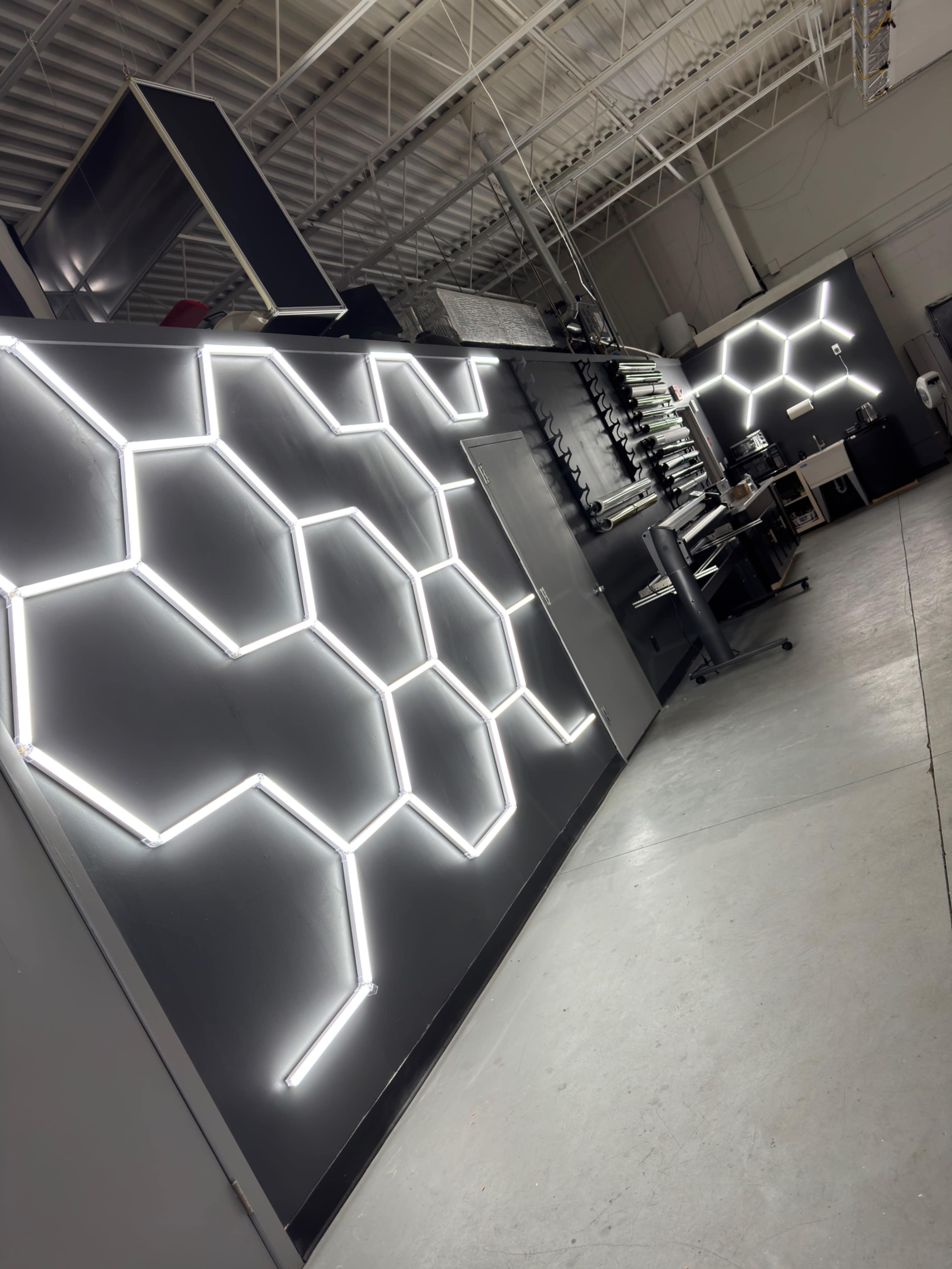 The image shows a wall with a hexagonal pattern illuminated by neon-like lighting in a spacious industrial setting.