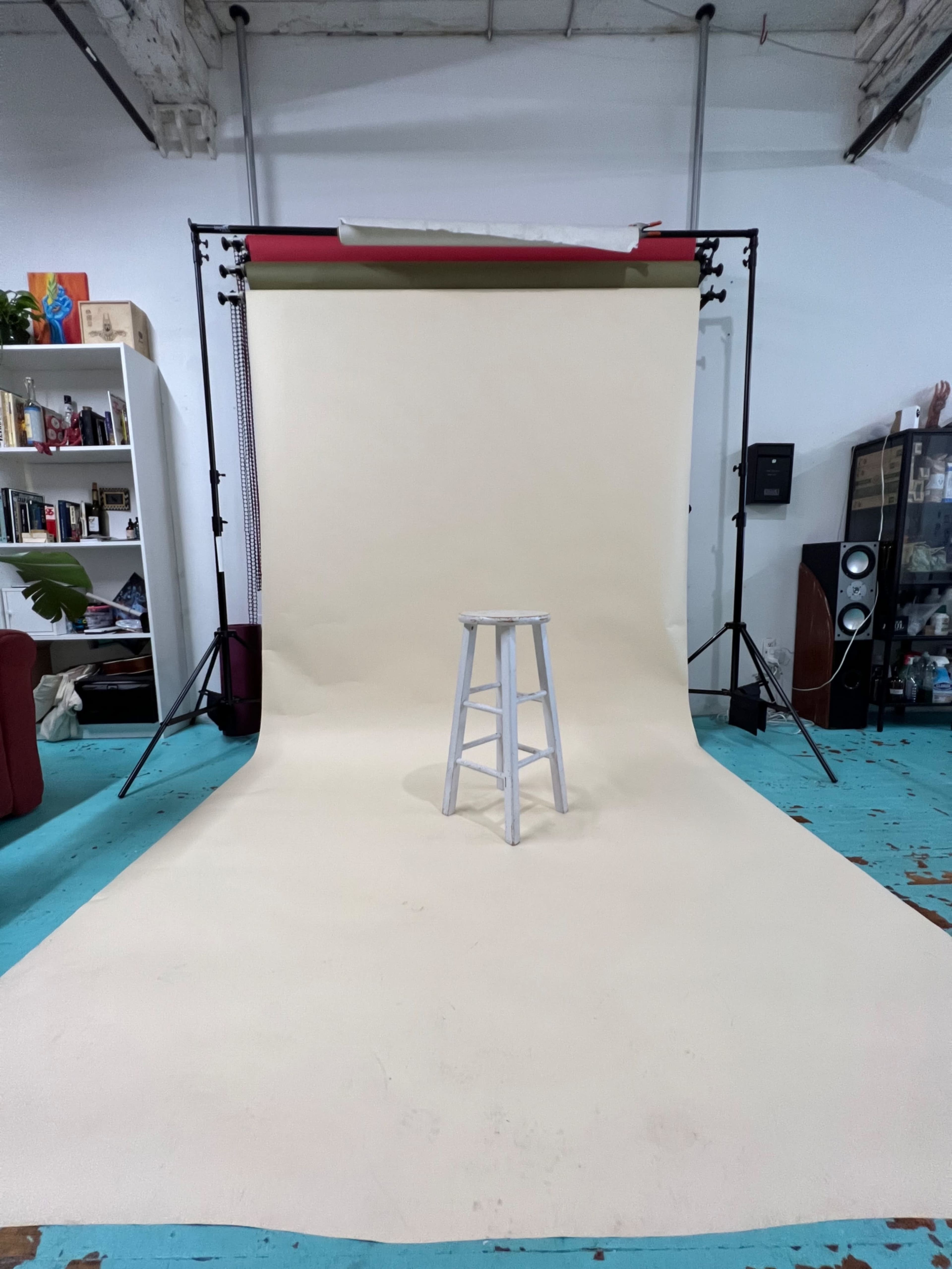 A white stool is positioned in front of a beige photography backdrop in a studio setting.