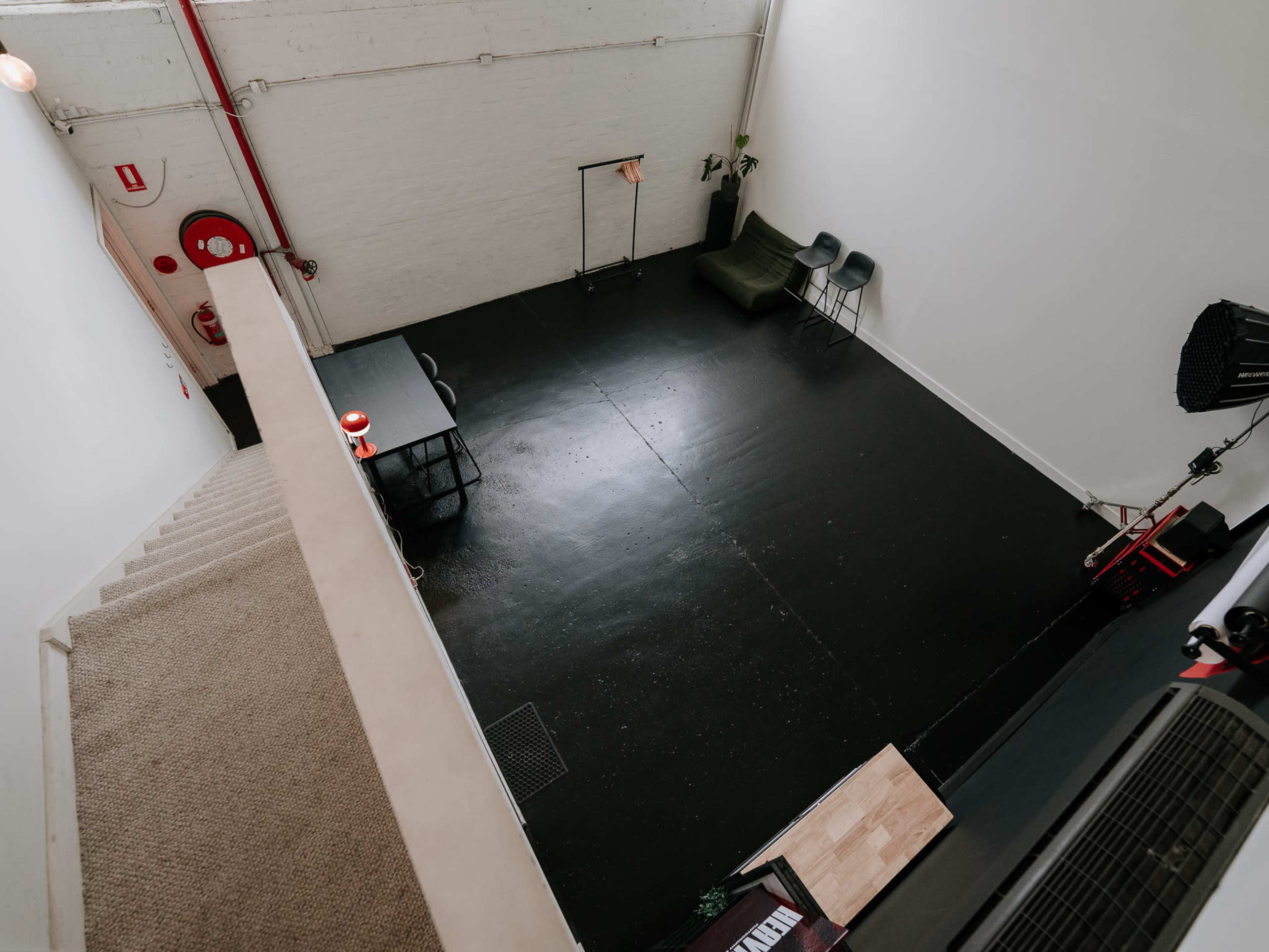 The image shows a spacious, minimalist studio with a black floor, a table, chairs, and a staircase in the foreground.