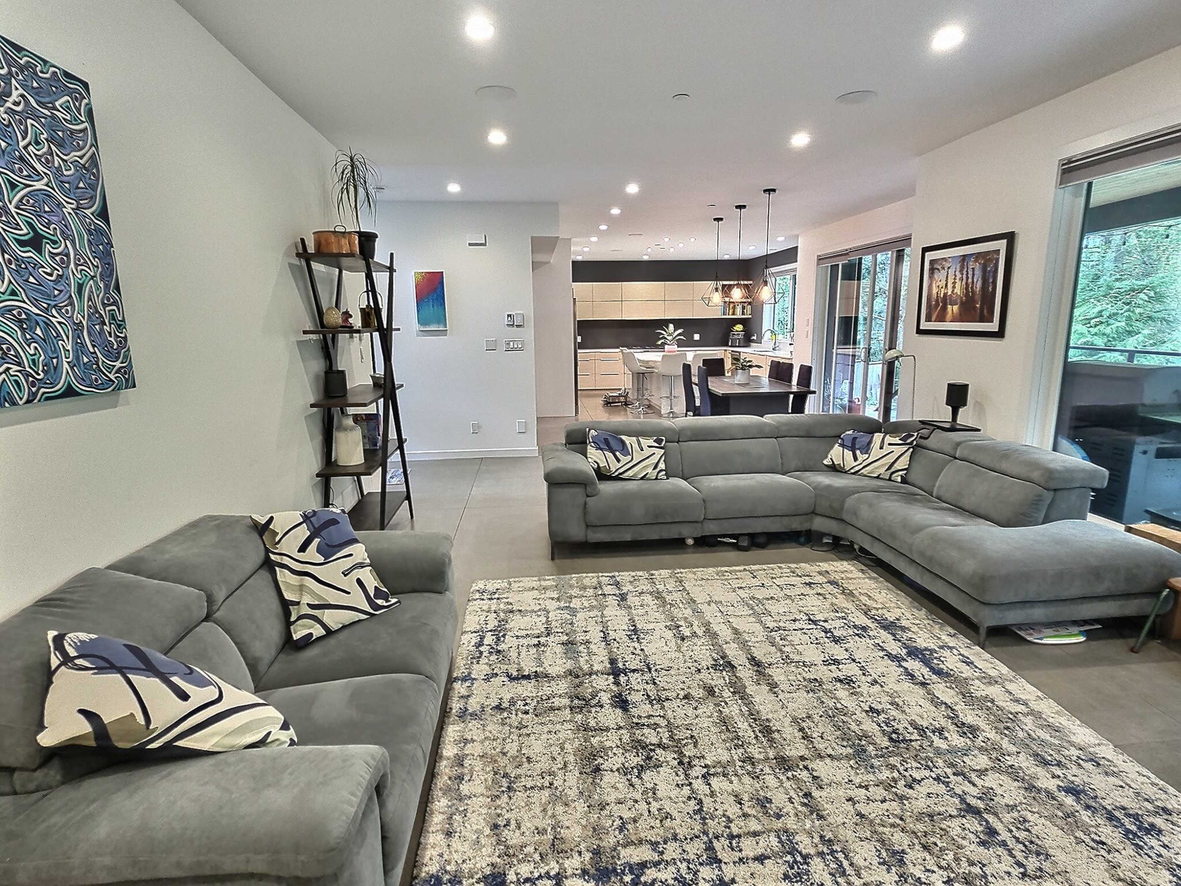 A modern living room with a sectional couch, a patterned rug, and an open layout leading to a kitchen area visible in the background.