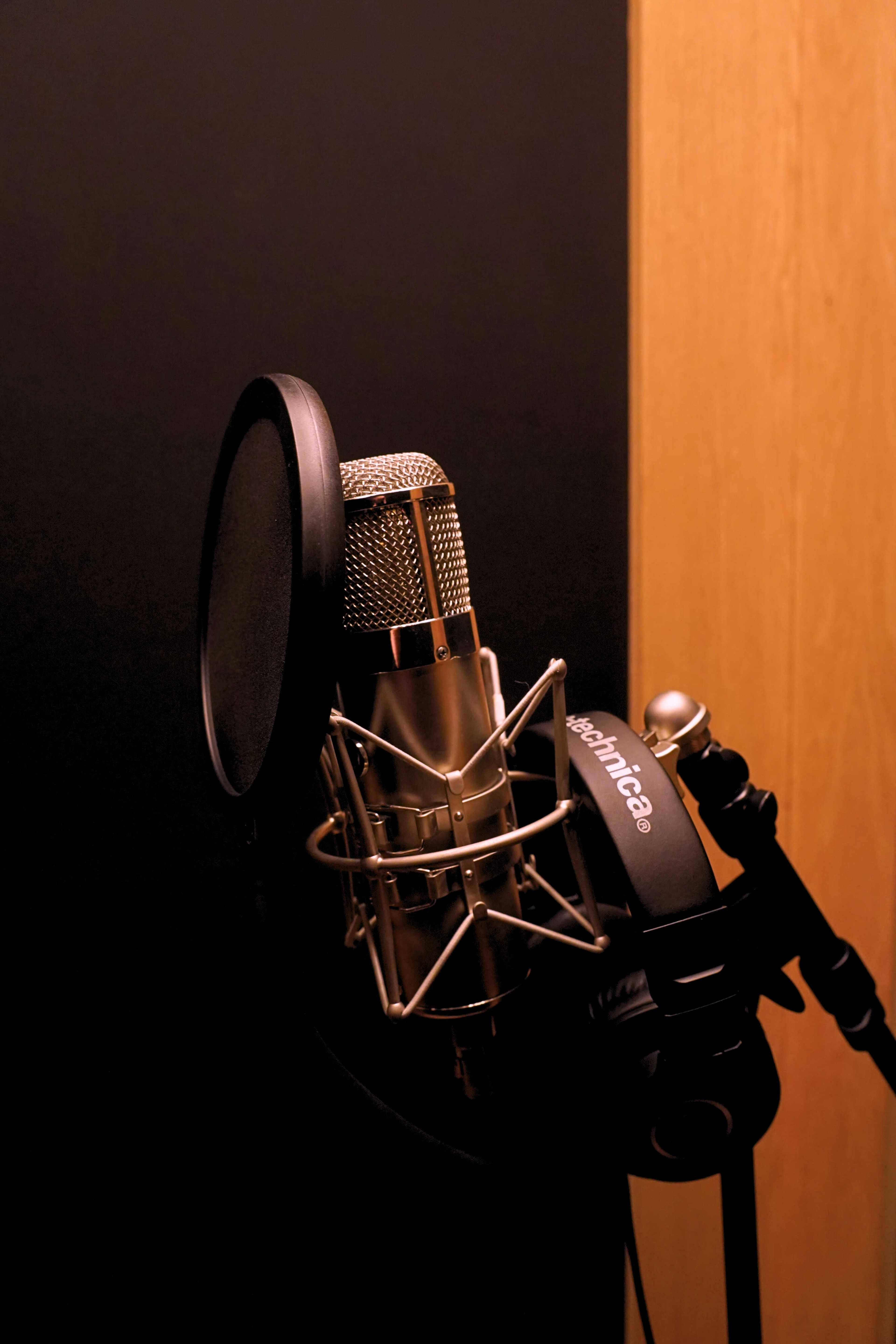 A microphone is positioned in a recording studio setting with a soundproof backdrop.