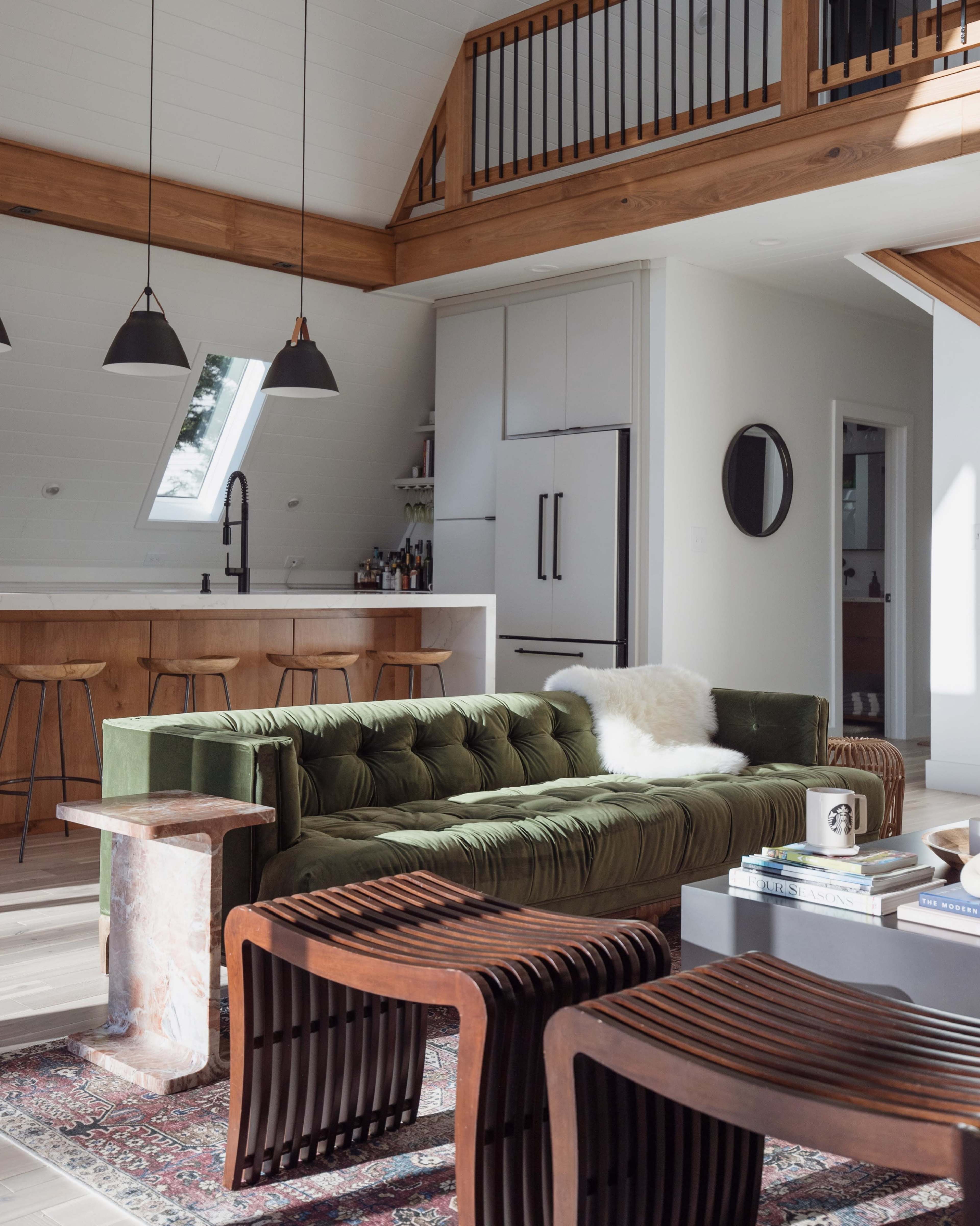The scene features a modern living area with a green velvet sofa, wooden accent furniture, and a minimalist kitchen in the background.