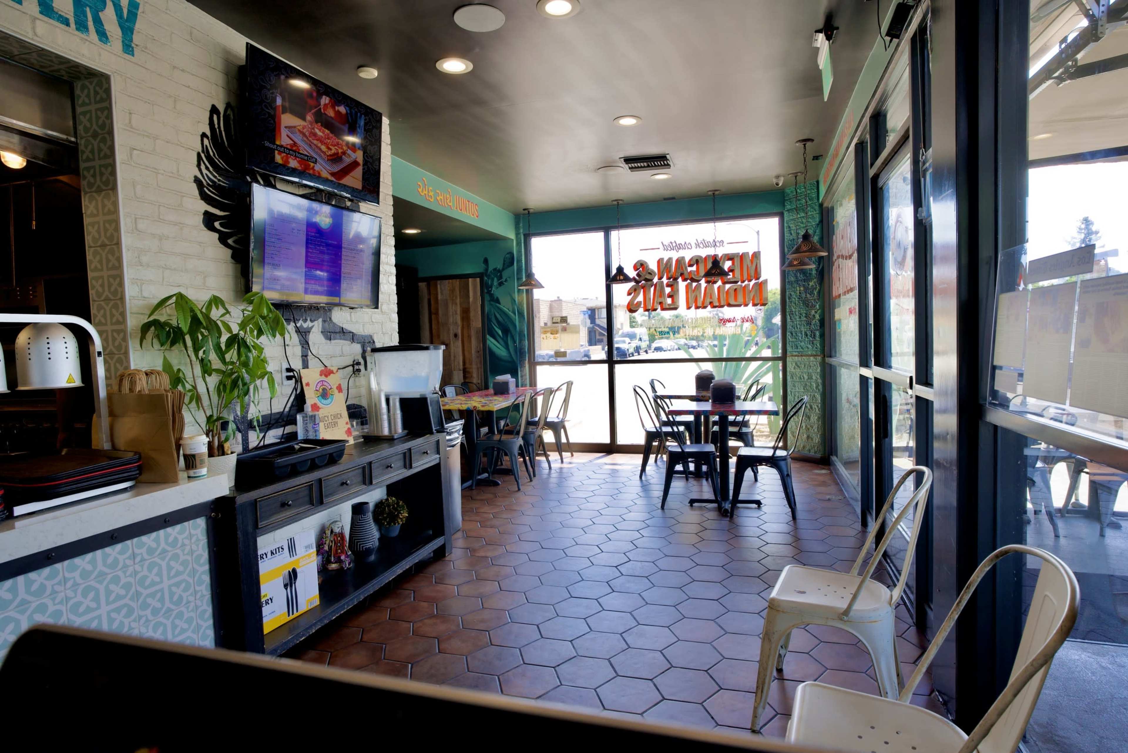 The image shows the interior of a casual restaurant with a seating area, counter, and large windows offering a view of the outside.