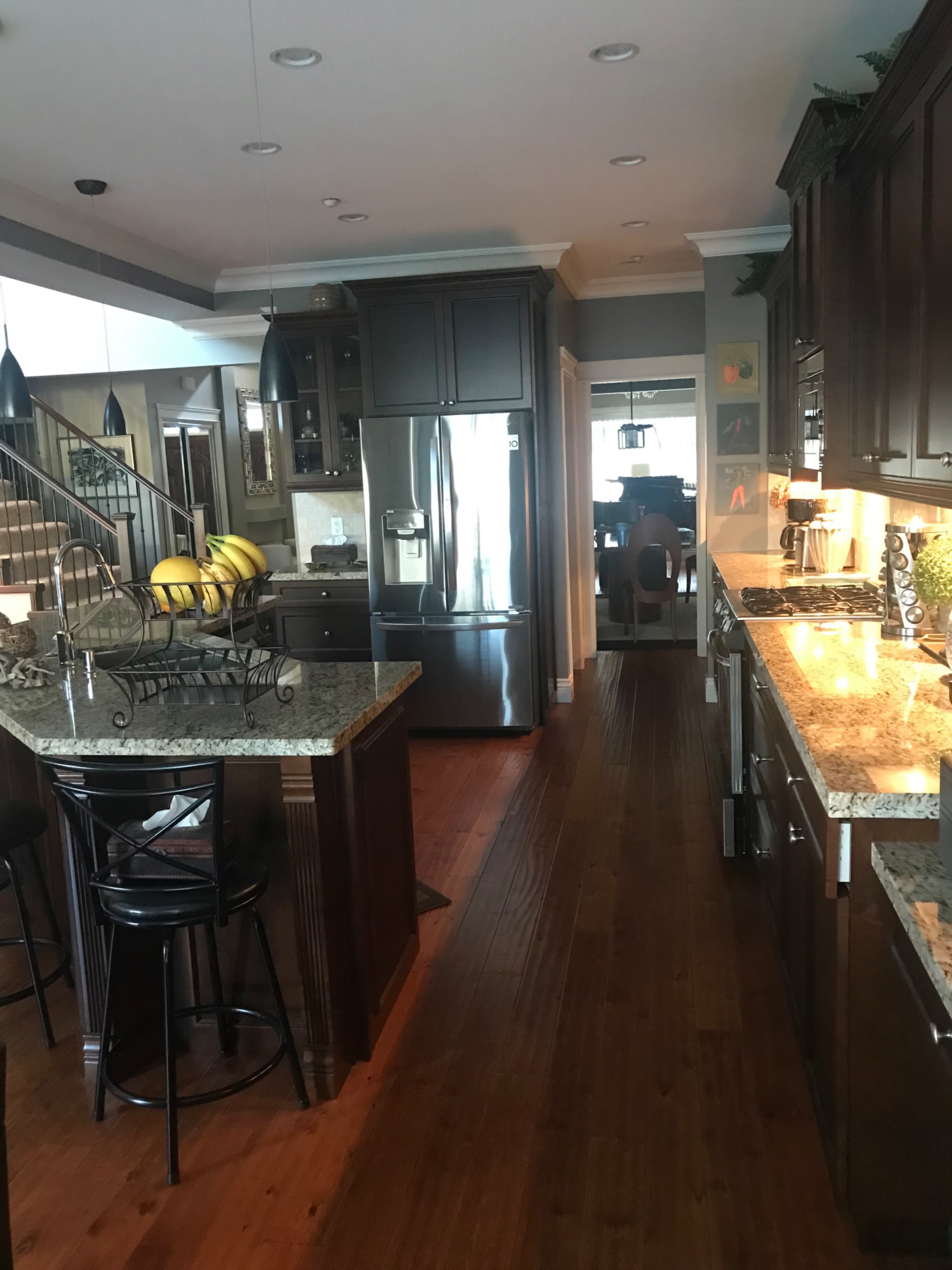 A modern kitchen with dark wooden cabinets, granite countertops, and a refrigerator next to a dining area.
