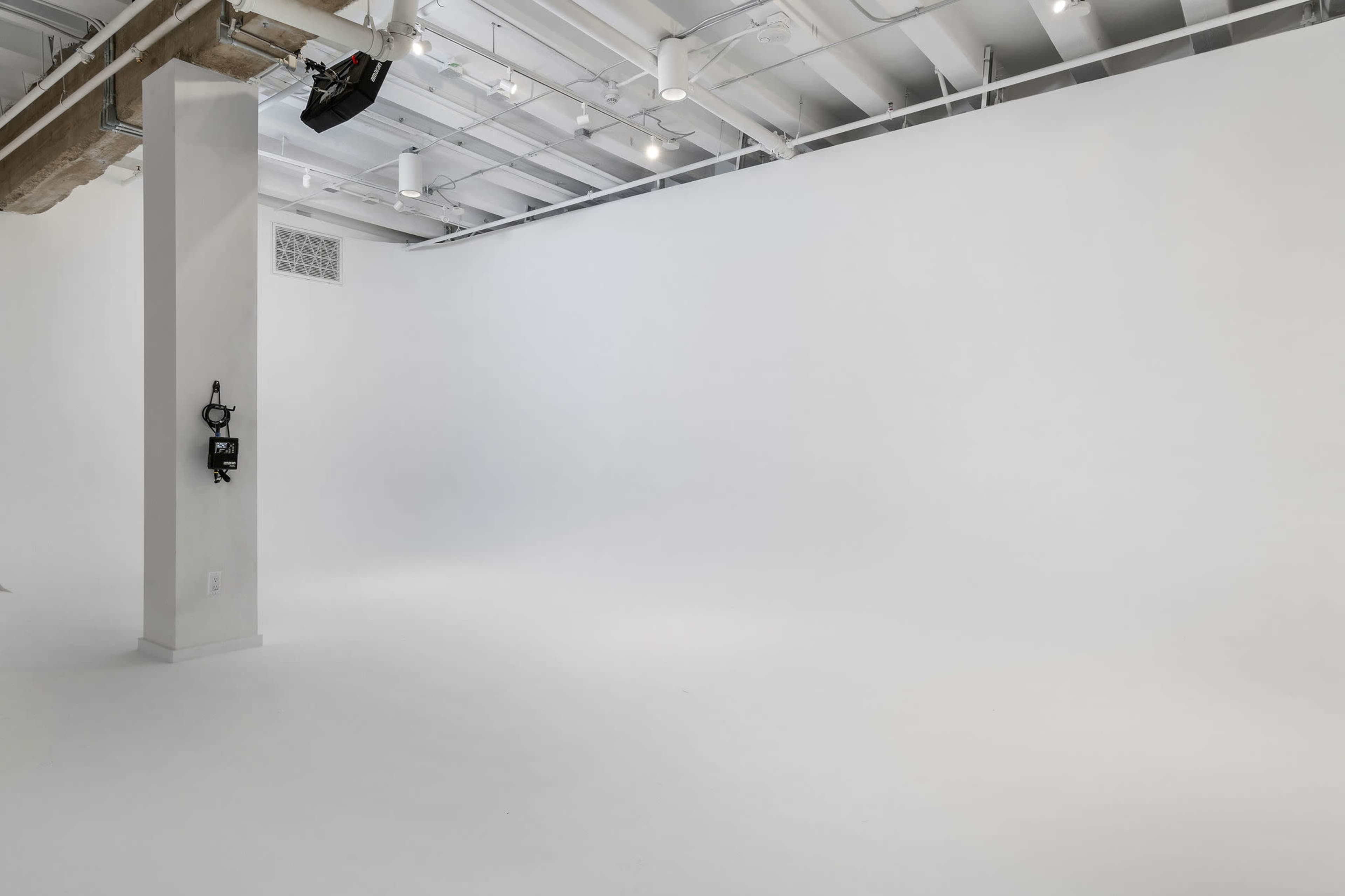 A spacious, empty studio with a white backdrop and exposed ceiling beams.
