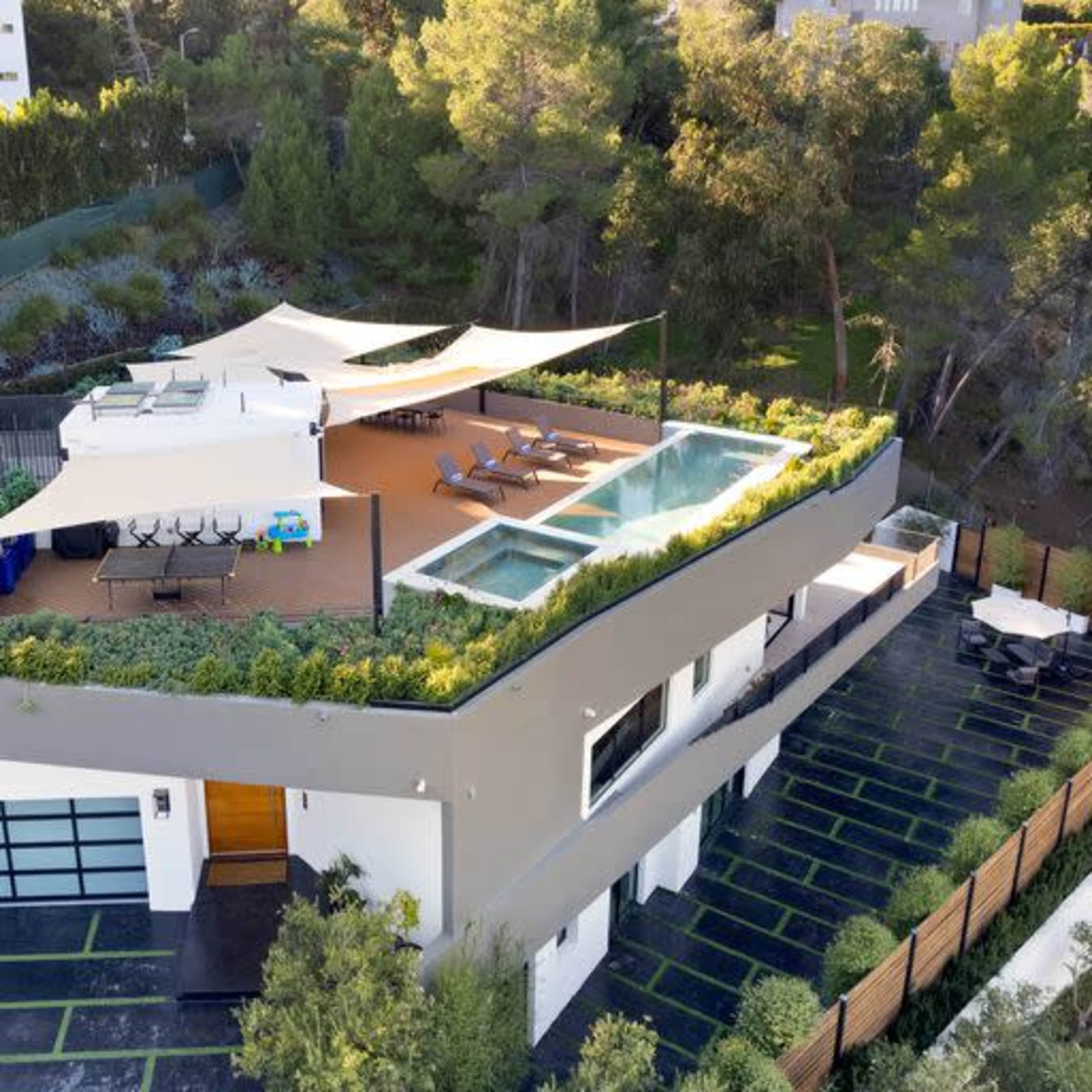 A modern house features multiple terraces, swimming pools, and landscaped areas surrounded by trees.
