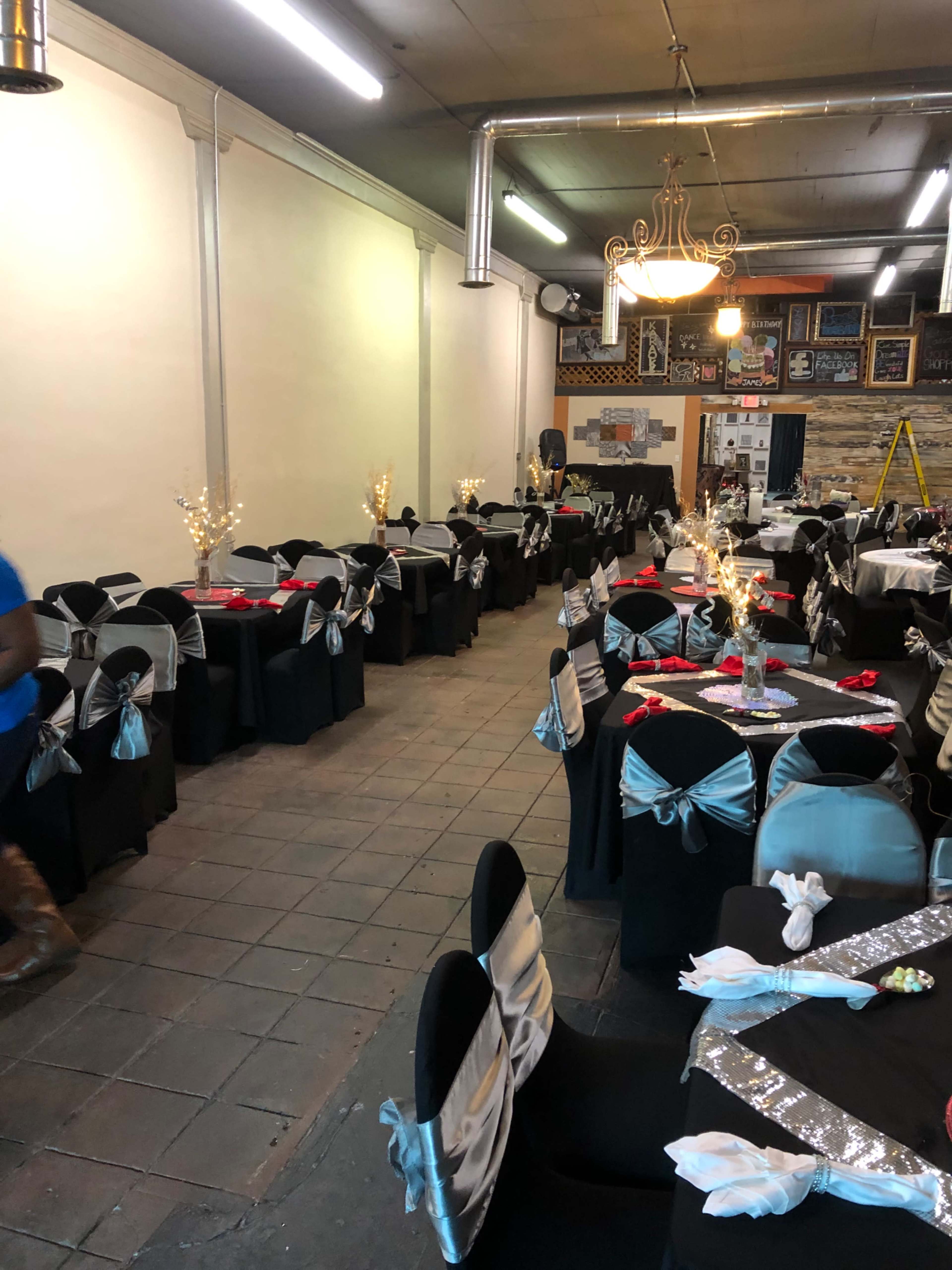 A banquet hall arranged with several tables covered in black tablecloths and decorated with silver and red accents.