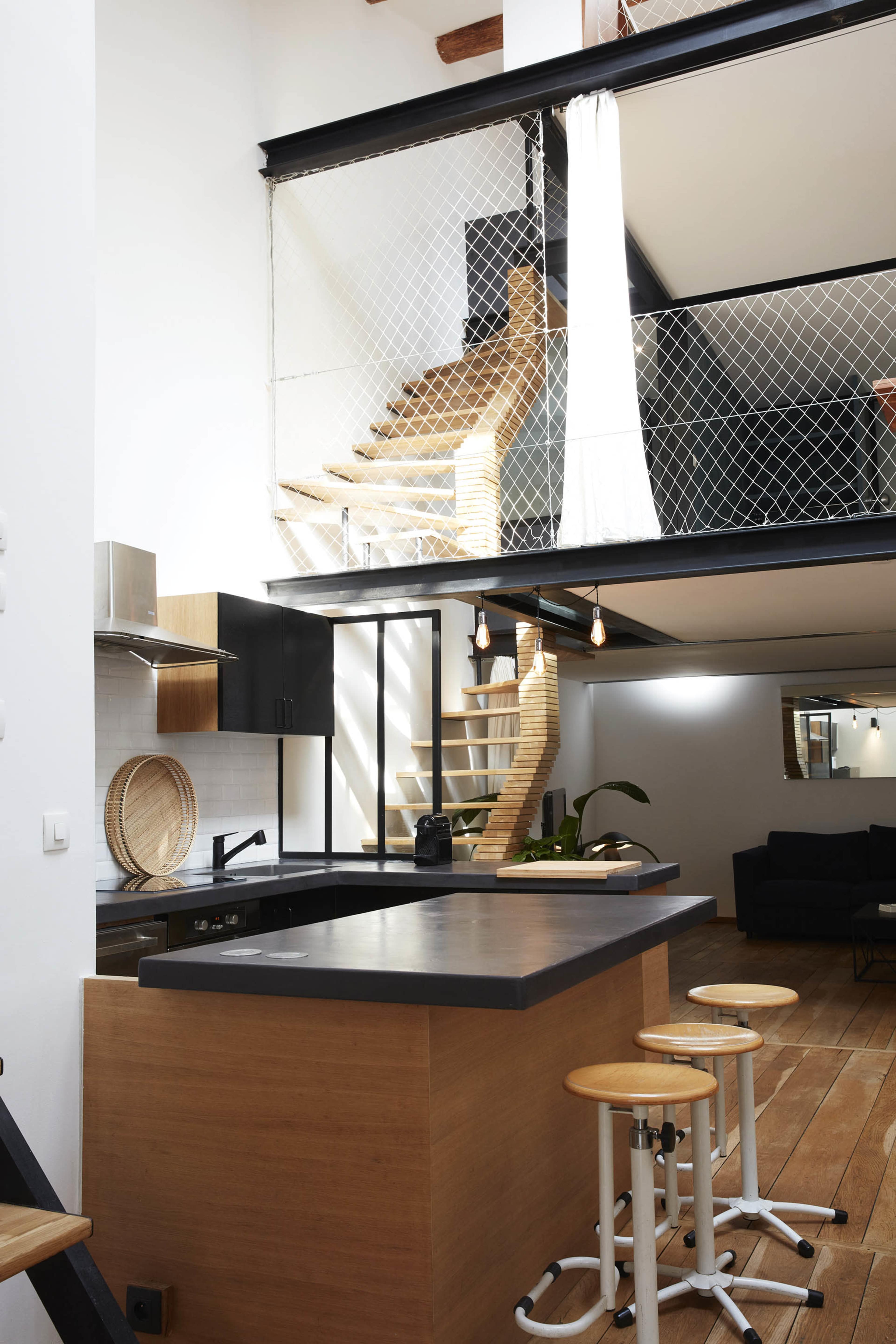 The image shows a modern kitchen with a wooden island, black cabinetry, and a staircase leading to an upper level enclosed by a net.