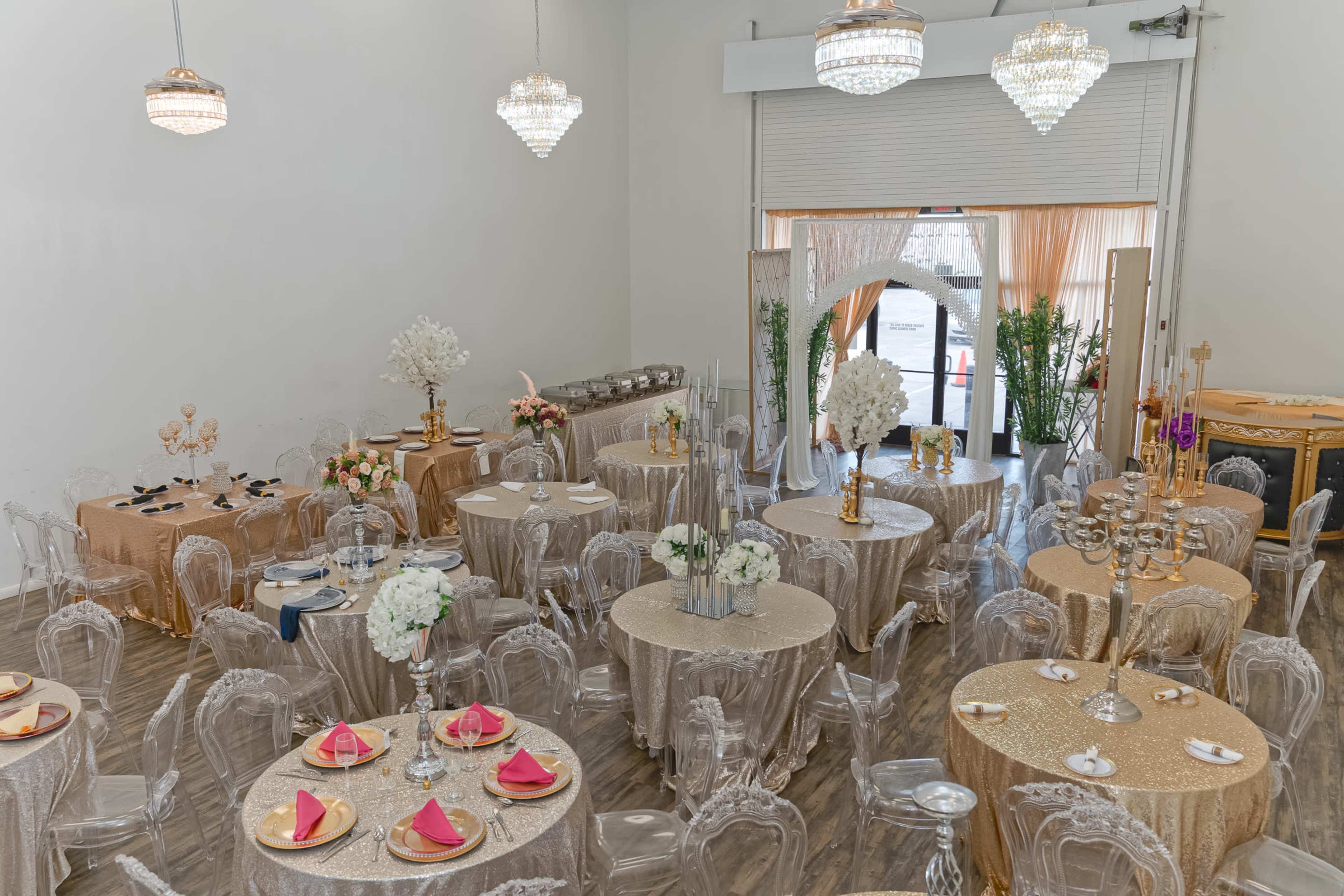 The image depicts an elegantly arranged banquet hall with round tables covered in gold tablecloths, adorned with floral centerpieces and crystal chandeliers hanging from the ceiling.