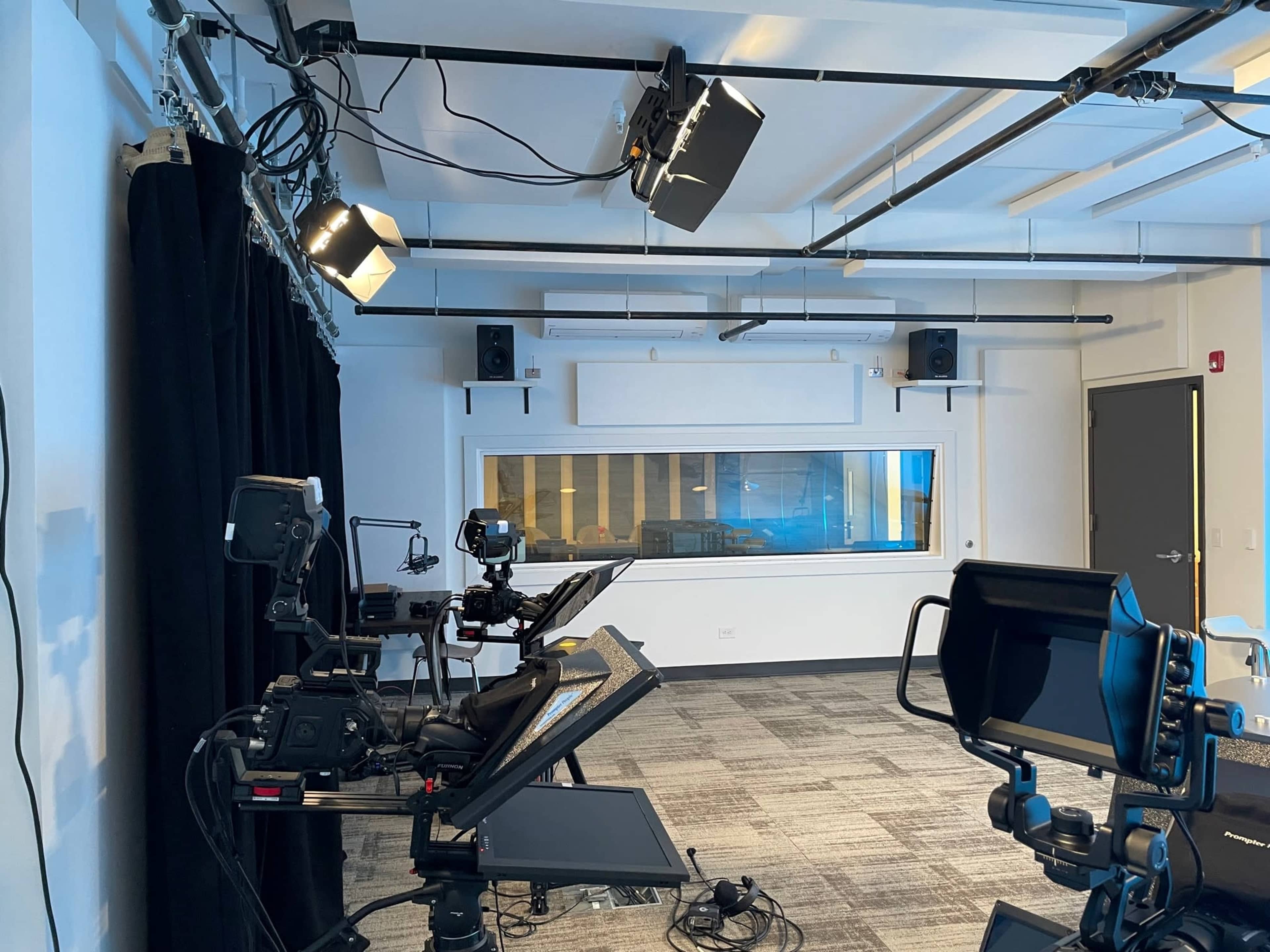 A modern recording studio equipped with cameras, lighting, and a soundproof glass booth.