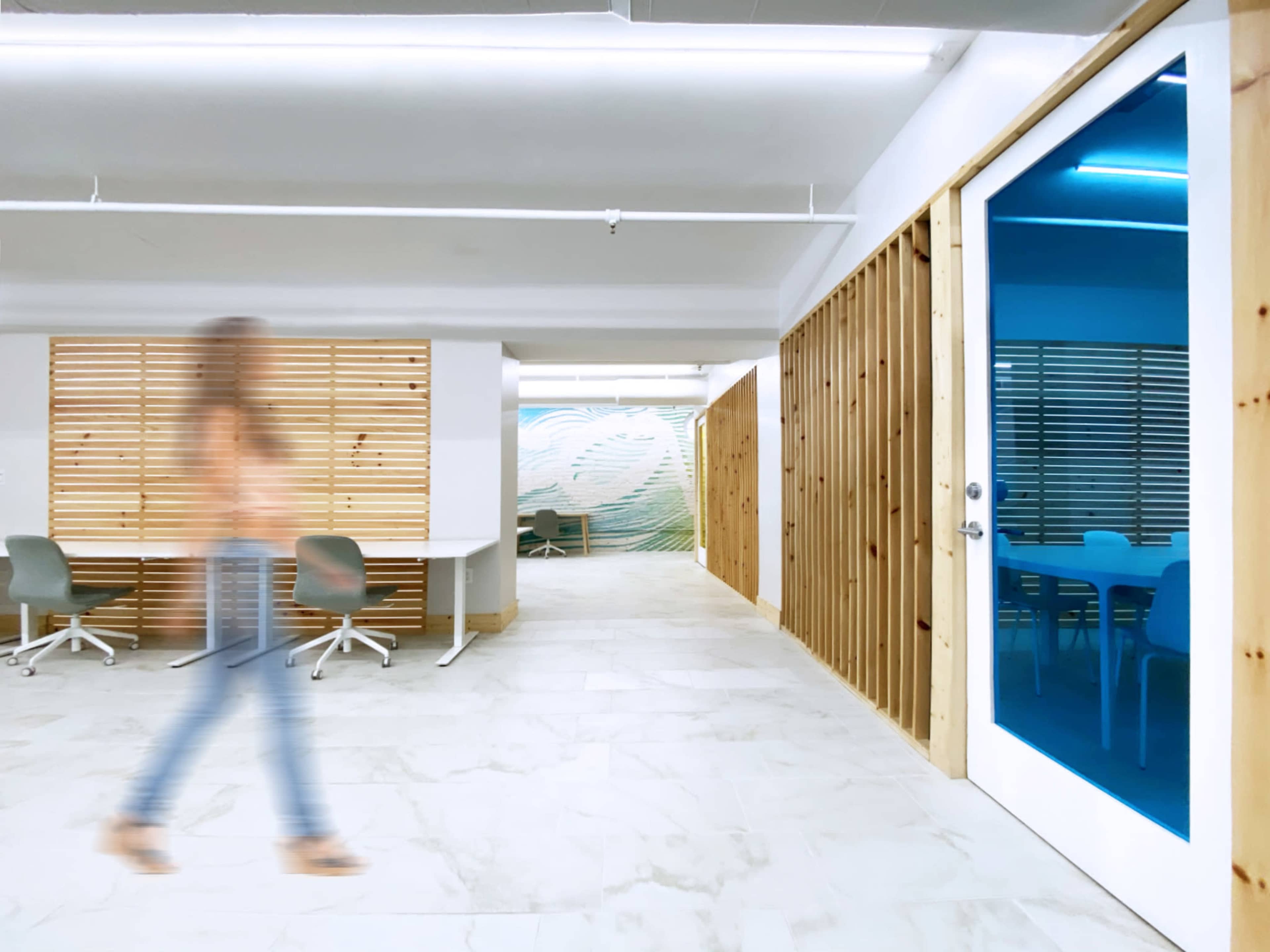 A person walks past a modern office space with wooden accents and a large mural on the wall.