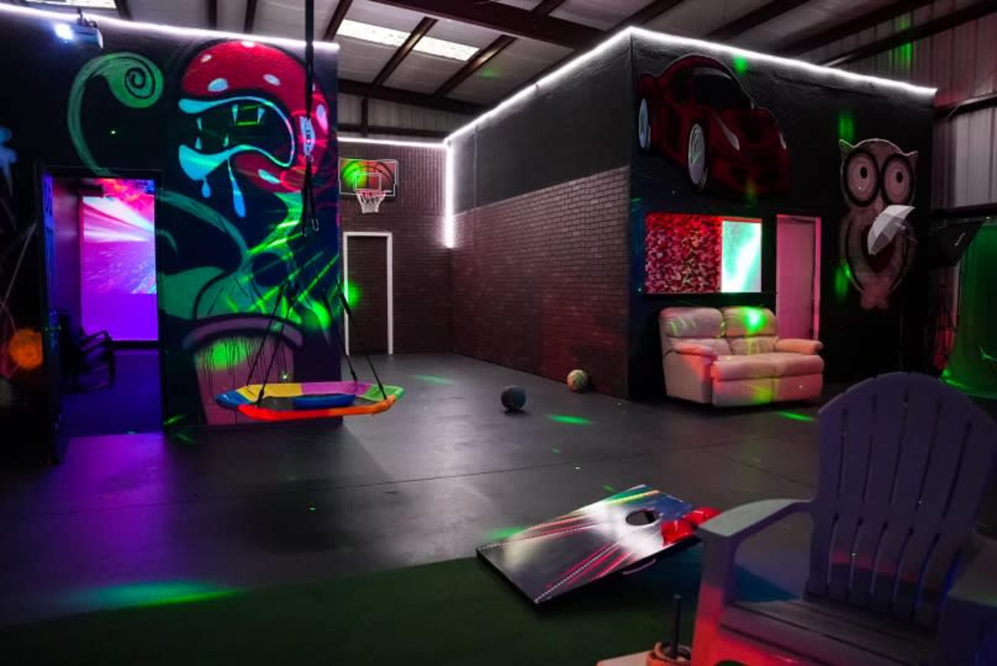 A vibrant indoor recreational space featuring colorful murals, a couch, a hanging swing, and various playful decorations illuminated by glowing lights.