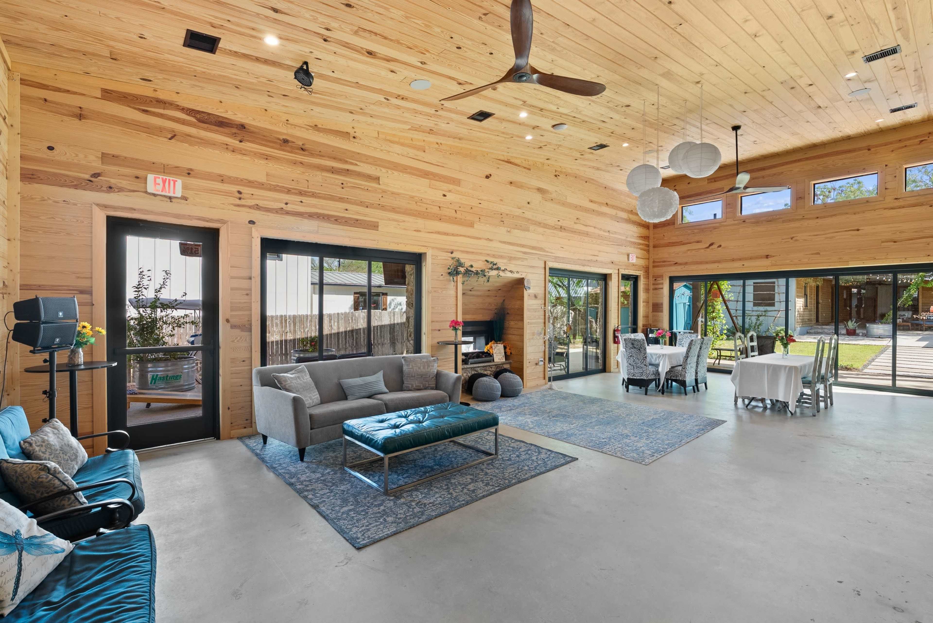 The interior of a modern, rustic-style gathering space features wooden walls, a concrete floor, and a seating area with a sofa, coffee table, and dining tables set up for events.