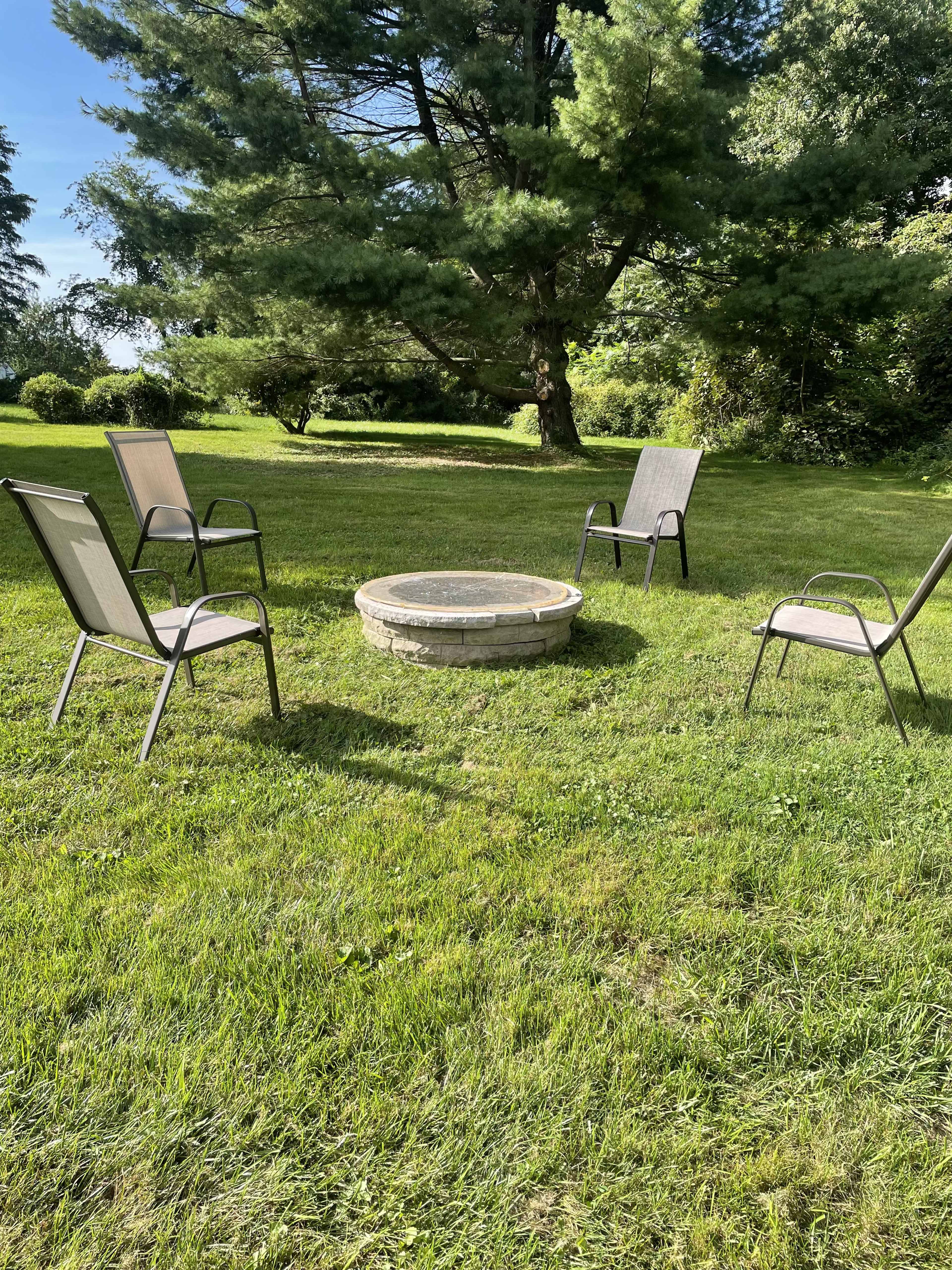 A stone fire pit surrounded by four metal chairs on a grassy lawn.