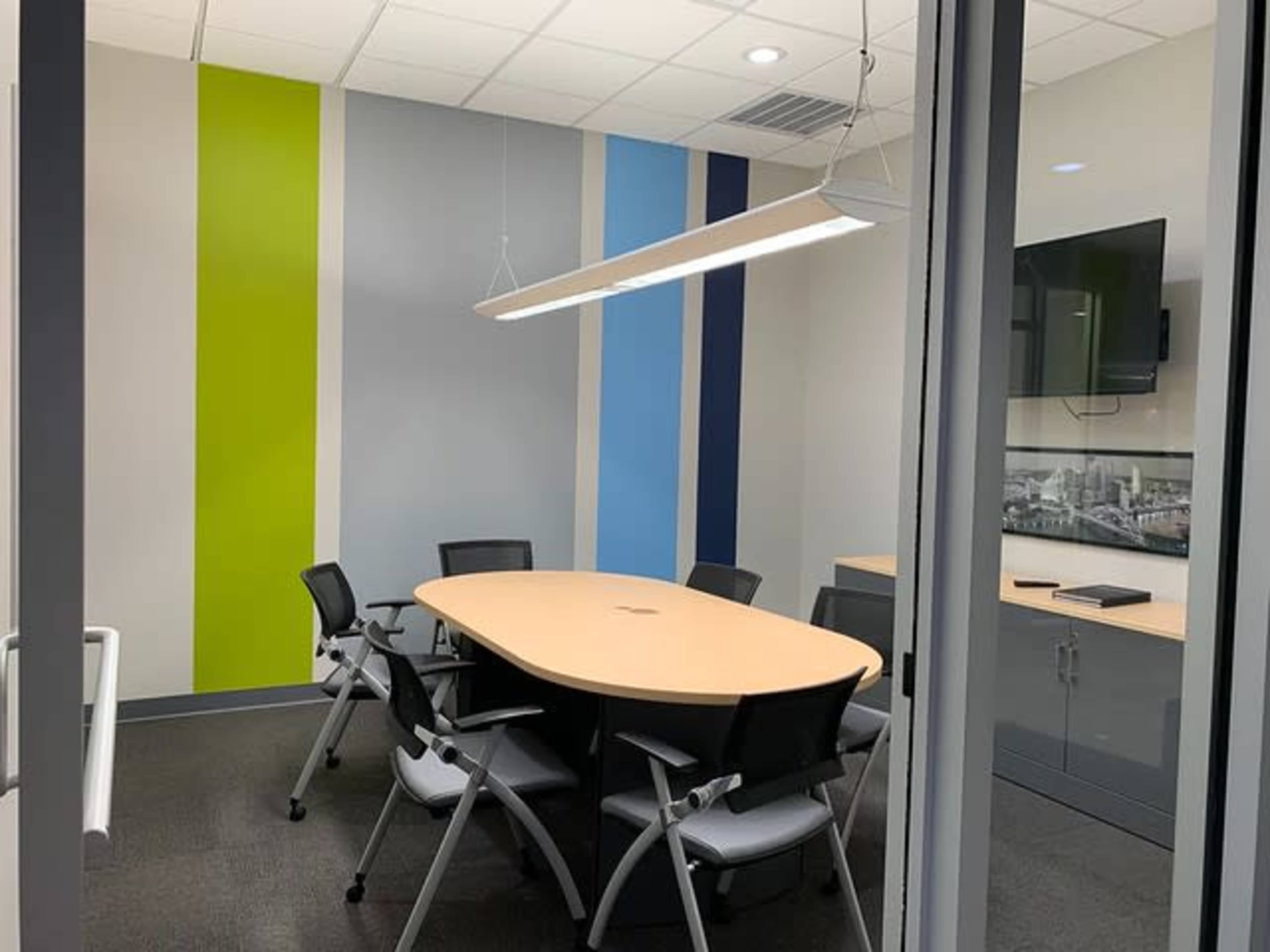A modern conference room with a round table surrounded by six chairs, featuring colorful accent walls in green and blue.