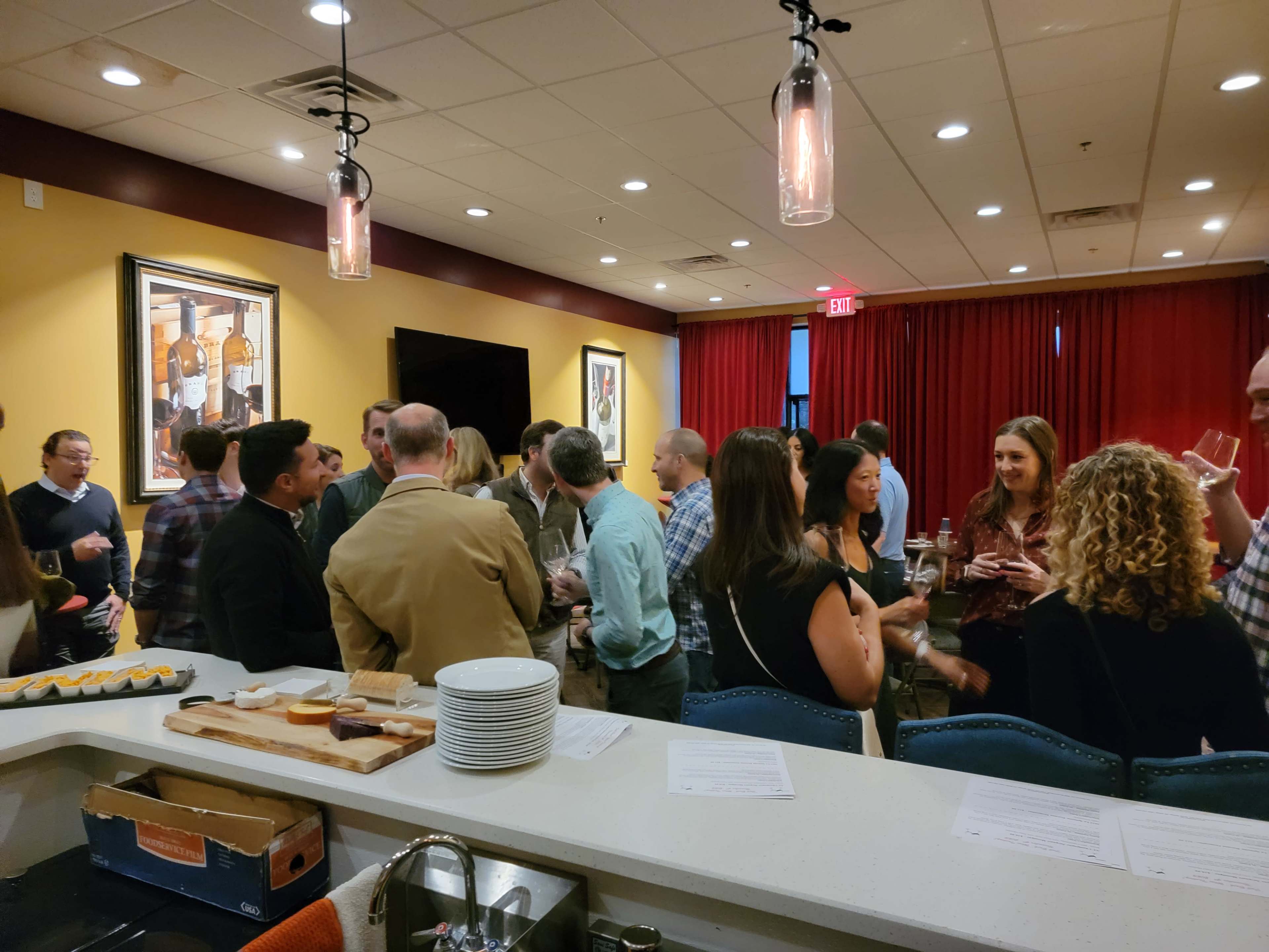 A group of people mingles at a social event in a well-lit room featuring warm colors and artwork on the walls.