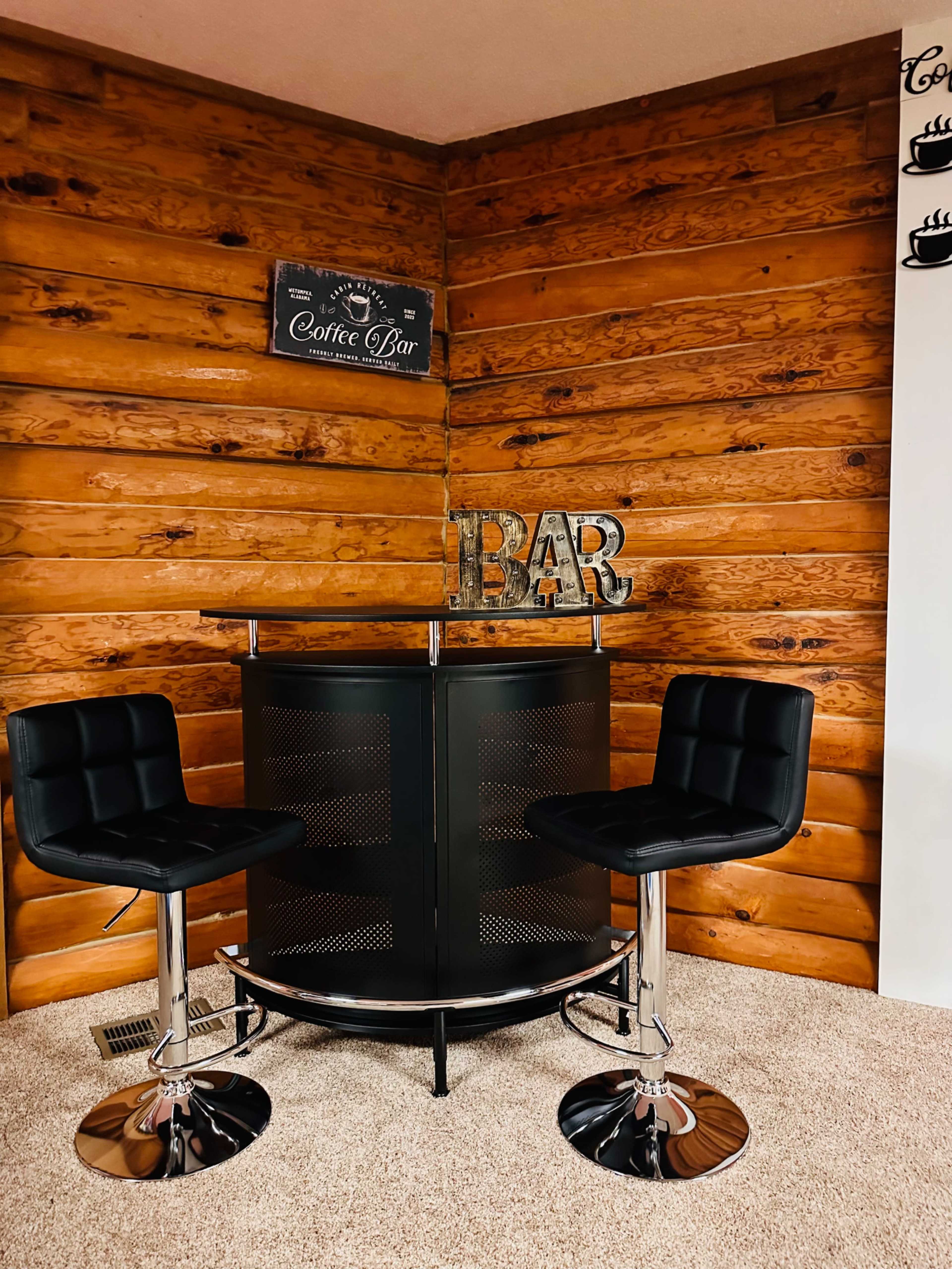 A small coffee bar with two black bar stools in a wooden-paneled room.