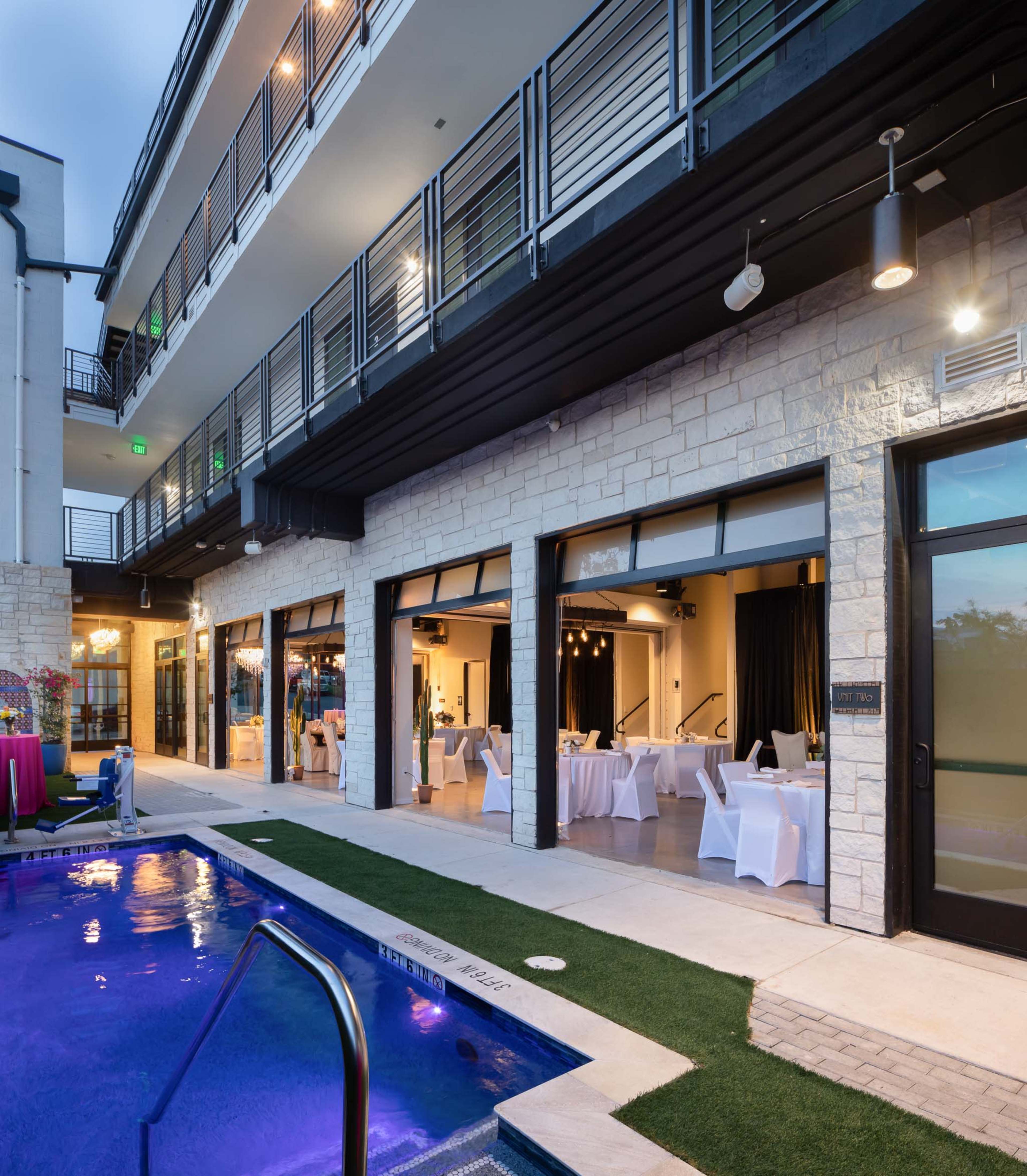 A modern building with a lounge area overlooking a pool, featuring large glass doors that open to a banquet room with tables set for dining.