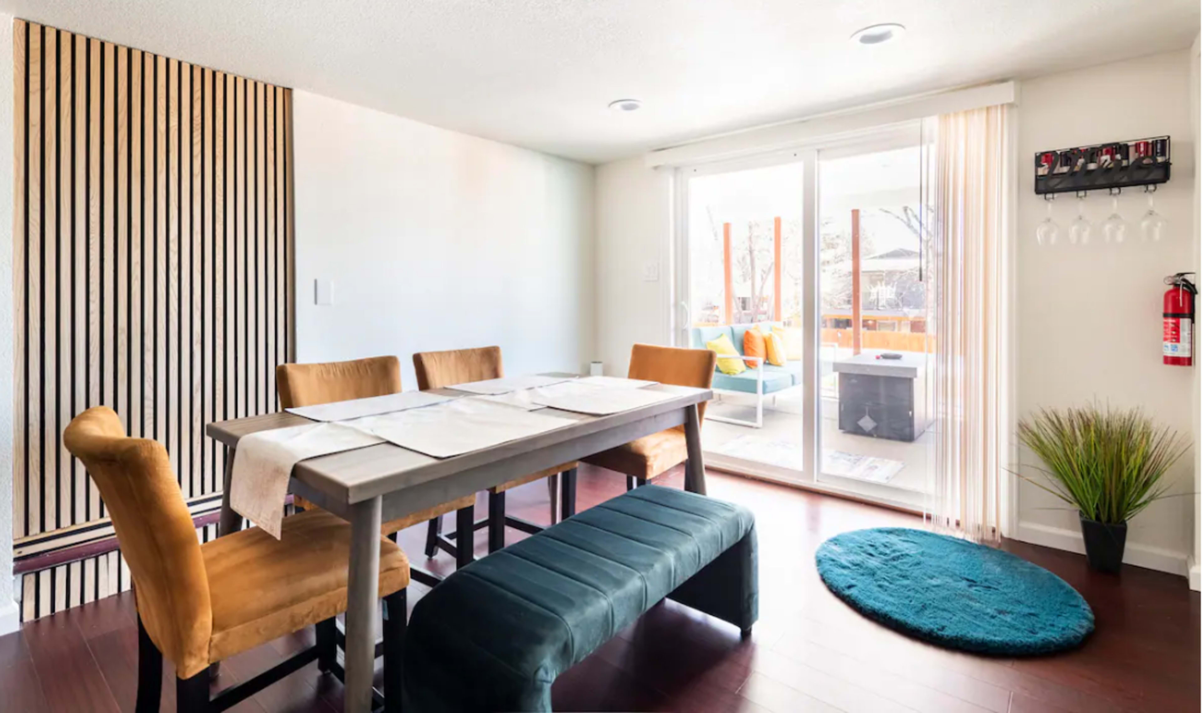 The dining area features a wooden table surrounded by chairs and a bench, with sliding glass doors leading to a patio.