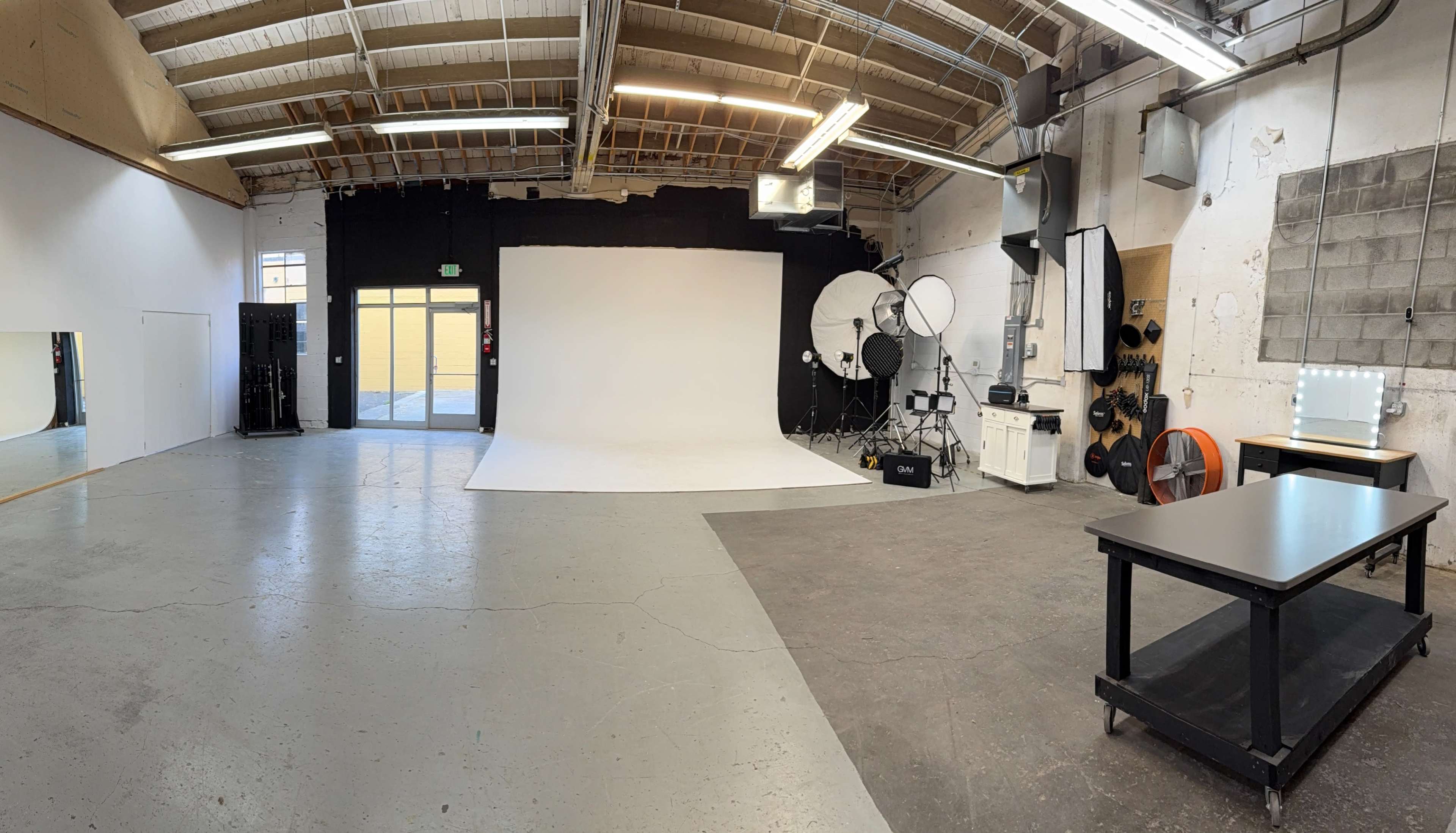 The image shows a spacious photography studio with a white backdrop, lighting equipment set up, and a table in the foreground.