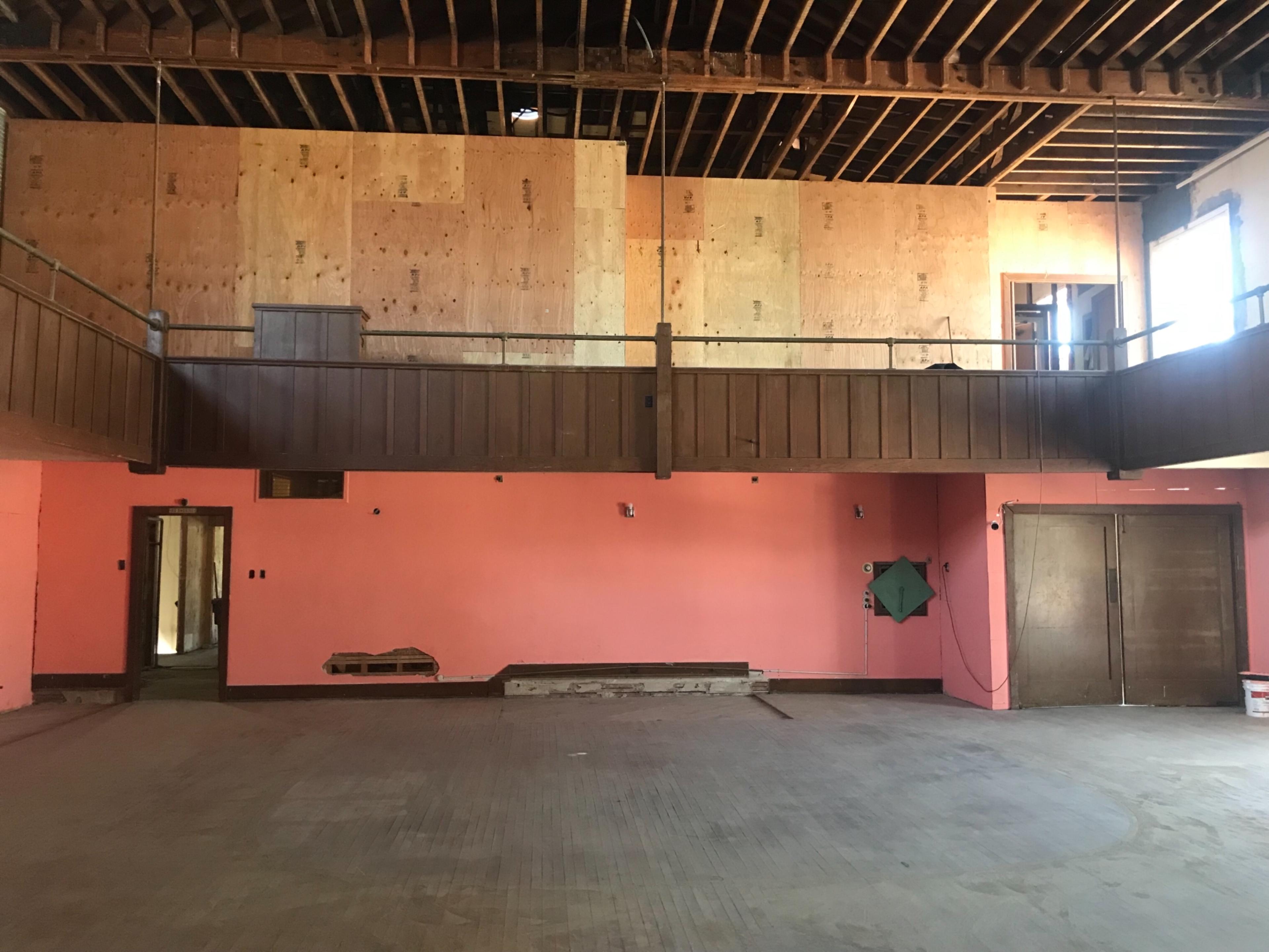 An unfinished interior space with exposed beams, plywood walls, and a pink-painted wall, featuring two doors and a balcony area.
