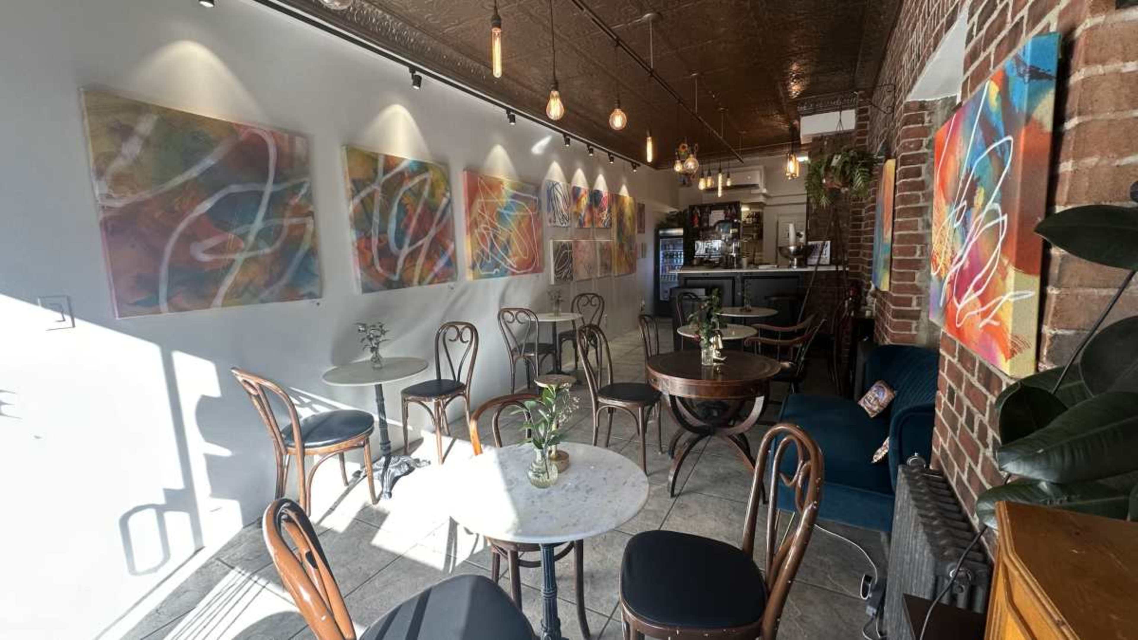 A cozy café interior with wooden tables, chairs, and colorful abstract paintings on the walls.