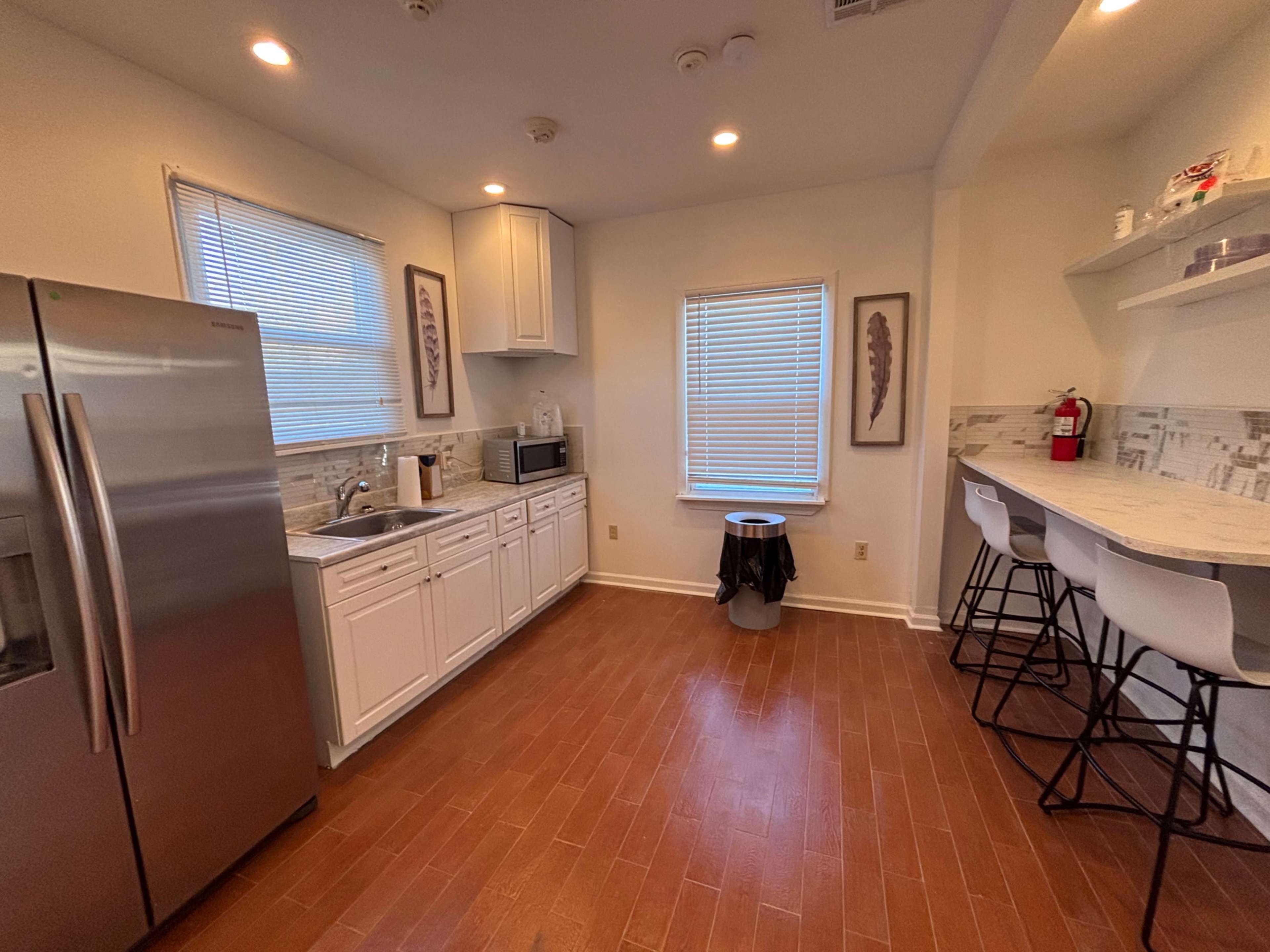 The image shows a modern kitchen featuring stainless steel appliances, white cabinetry, and a bar area with stools.