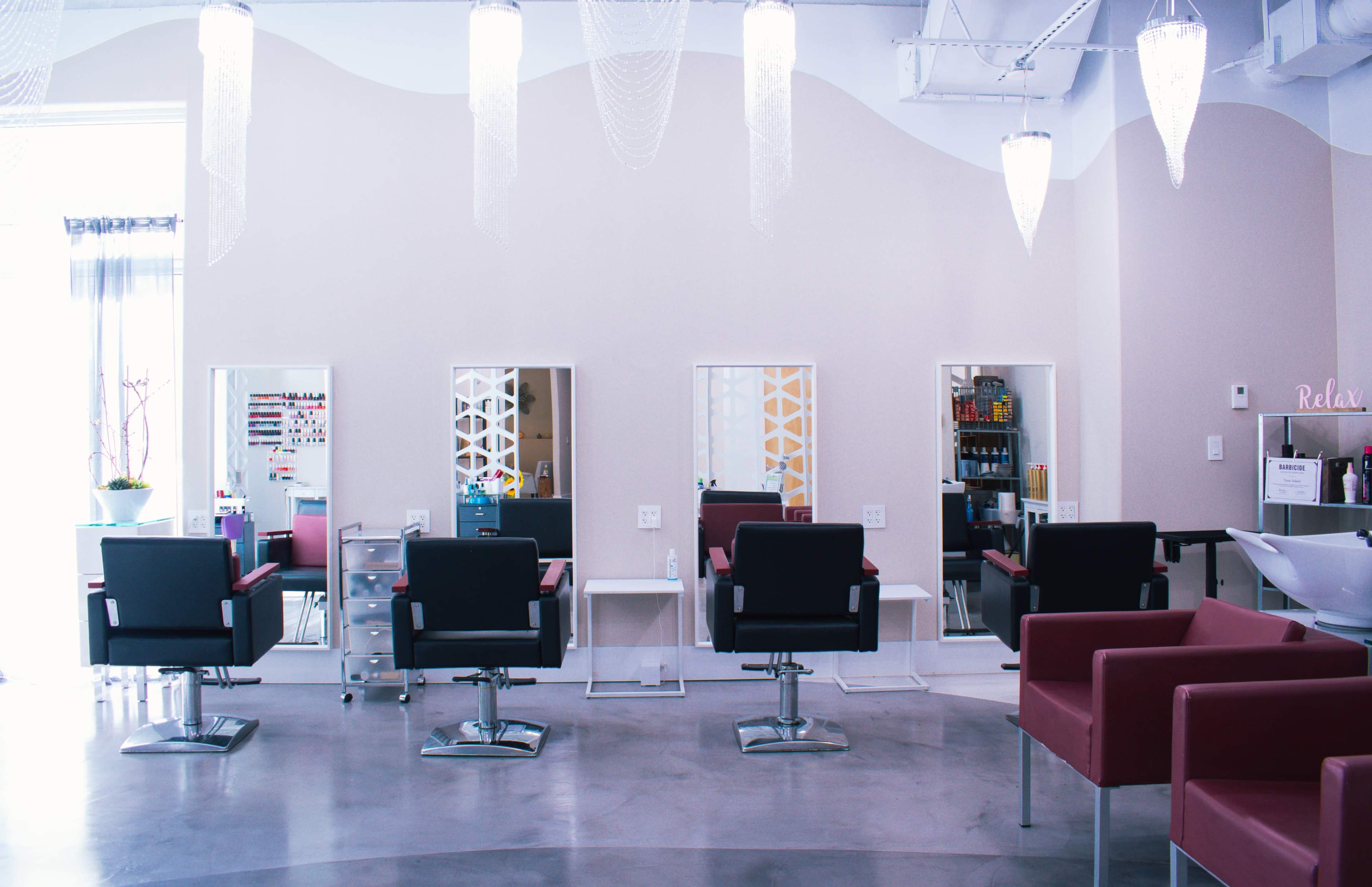 A modern hair salon with four styling stations, each equipped with a chair and mirror, alongside a salon sink area.