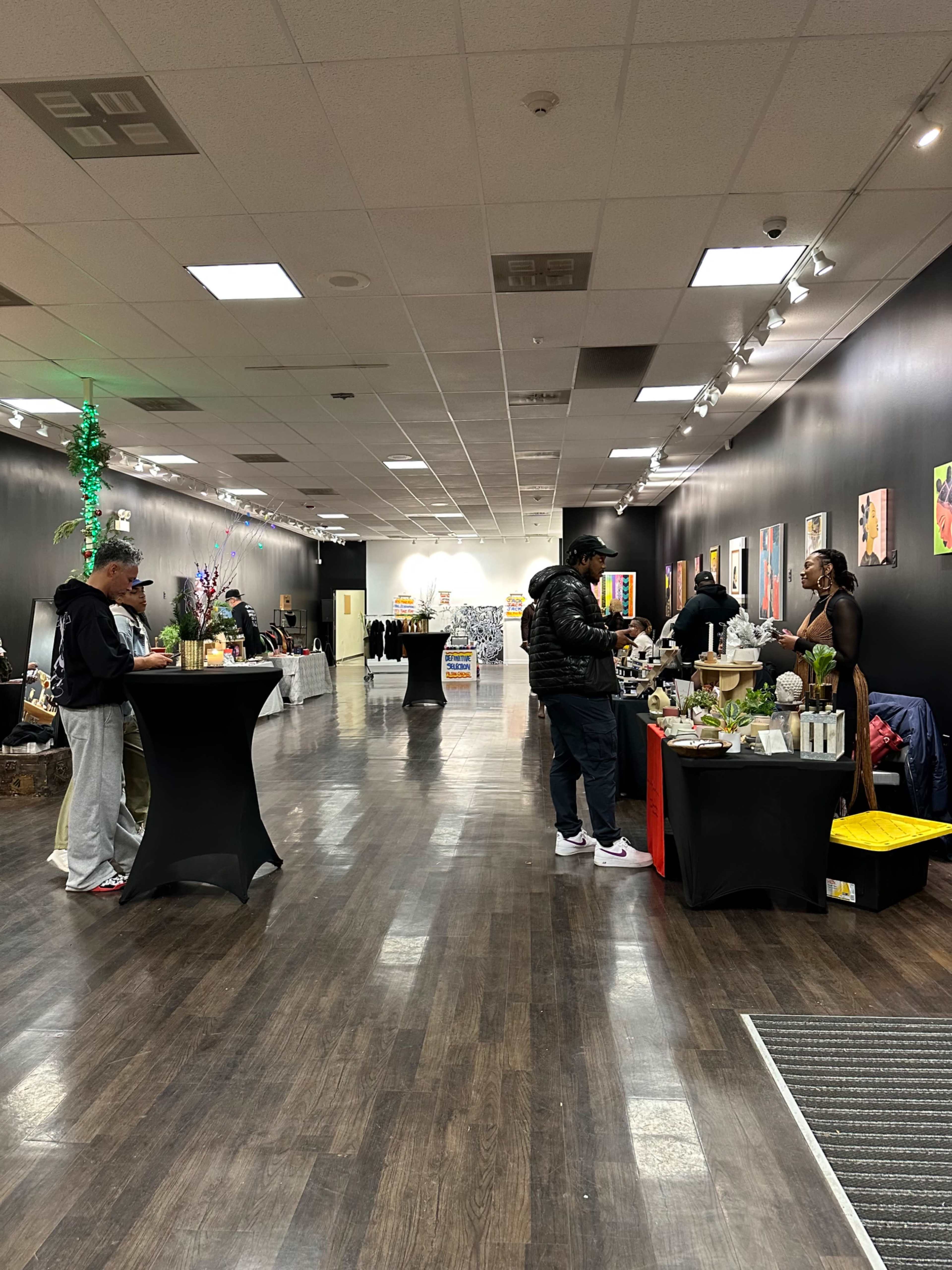 A spacious indoor market with various vendor tables on either side and people interacting among them.