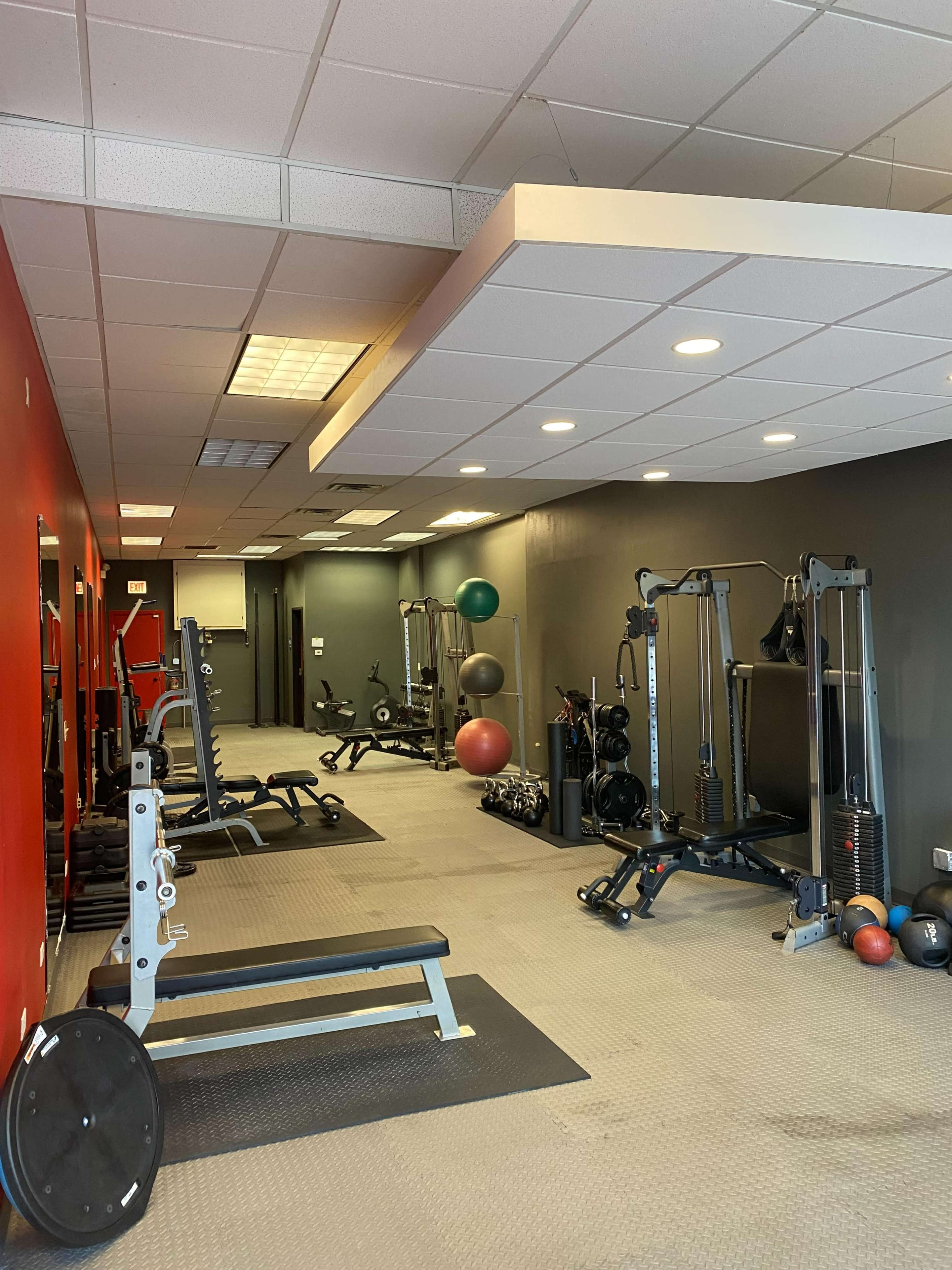 A gym interior with various exercise equipment, including weight benches, resistance machines, and exercise balls, against a backdrop of red and gray walls.