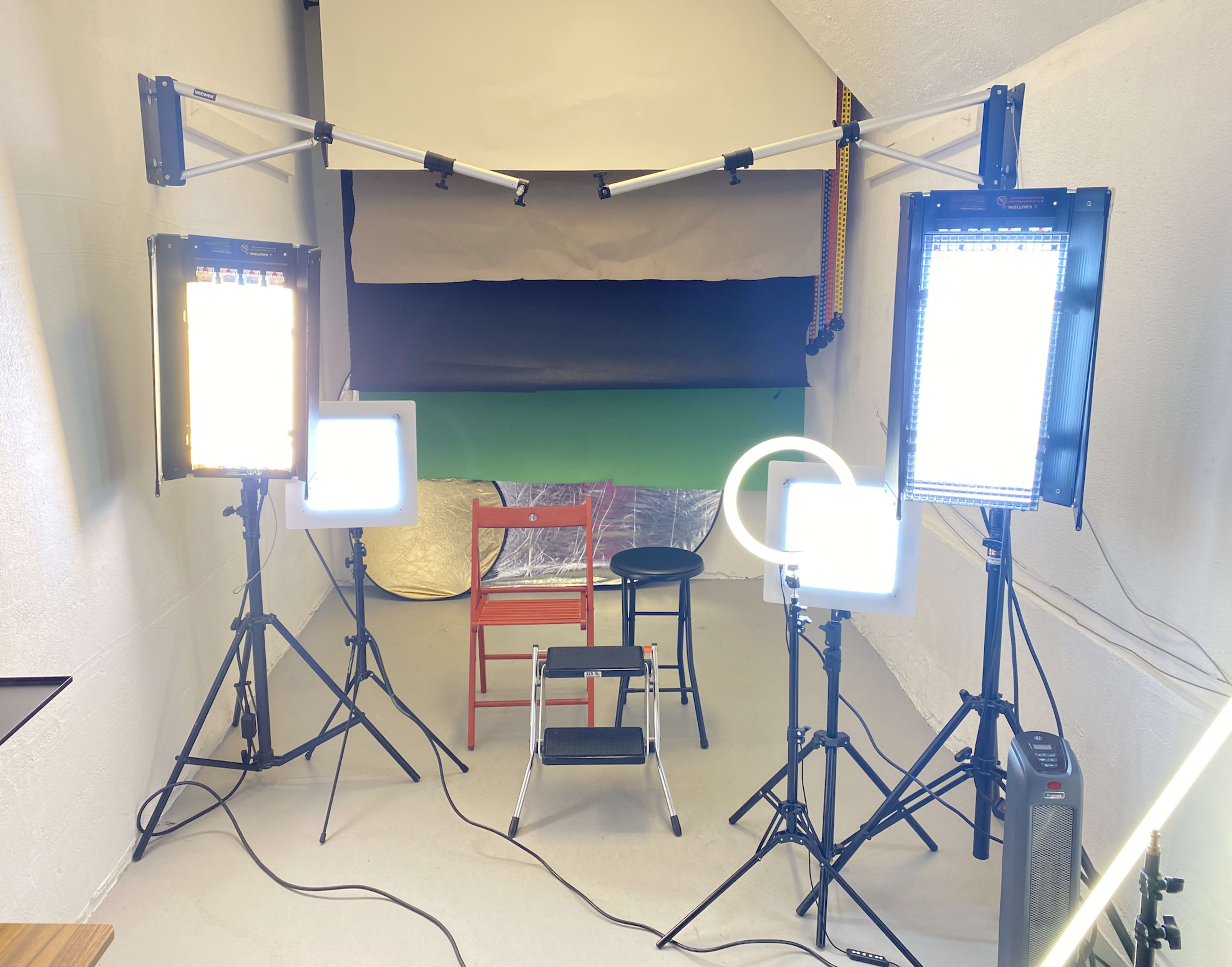 A photo studio setup with multiple LED lights, a red chair, a black stool, and a green backdrop.