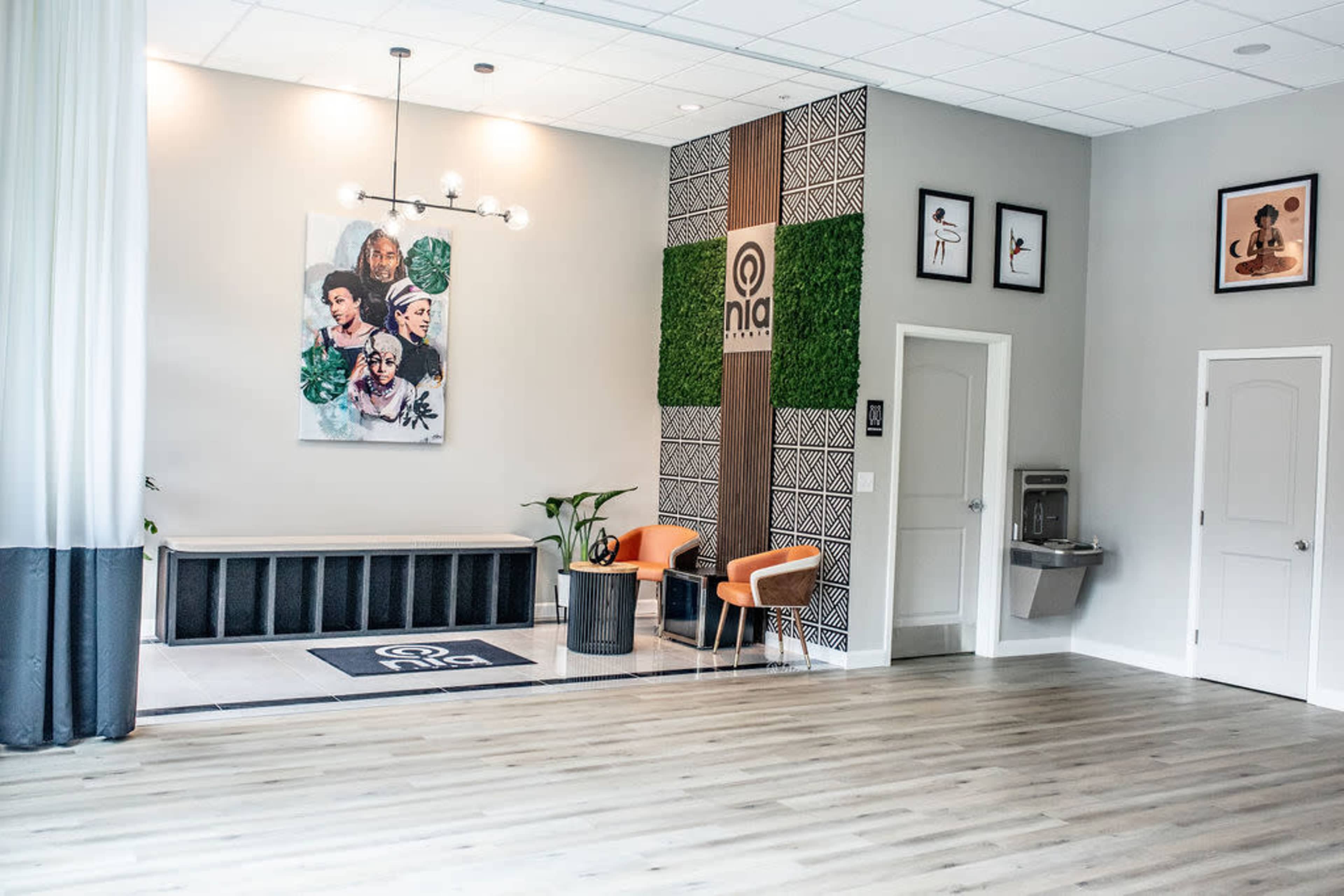 A modern interior space featuring a seating area with two orange chairs, decorative wall art, and a green plant against a stylish backdrop.