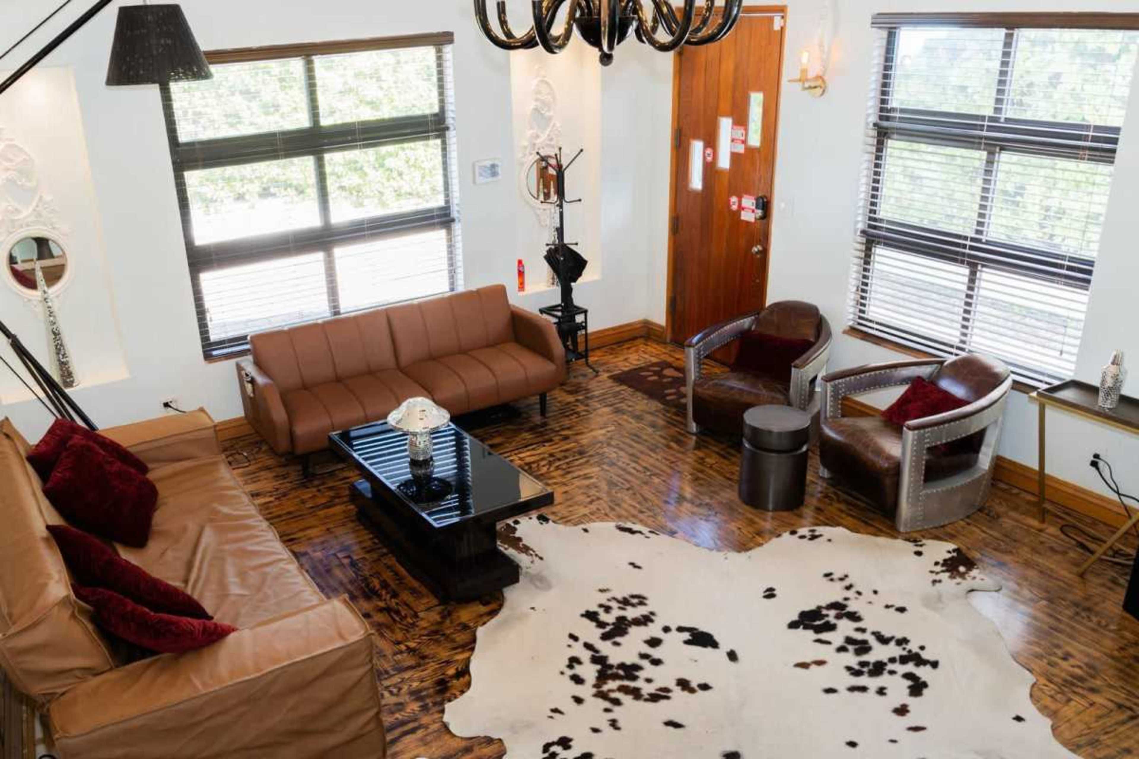 The image shows a cozy living room with brown sofas, two armchairs, a coffee table, and large windows that provide natural light.