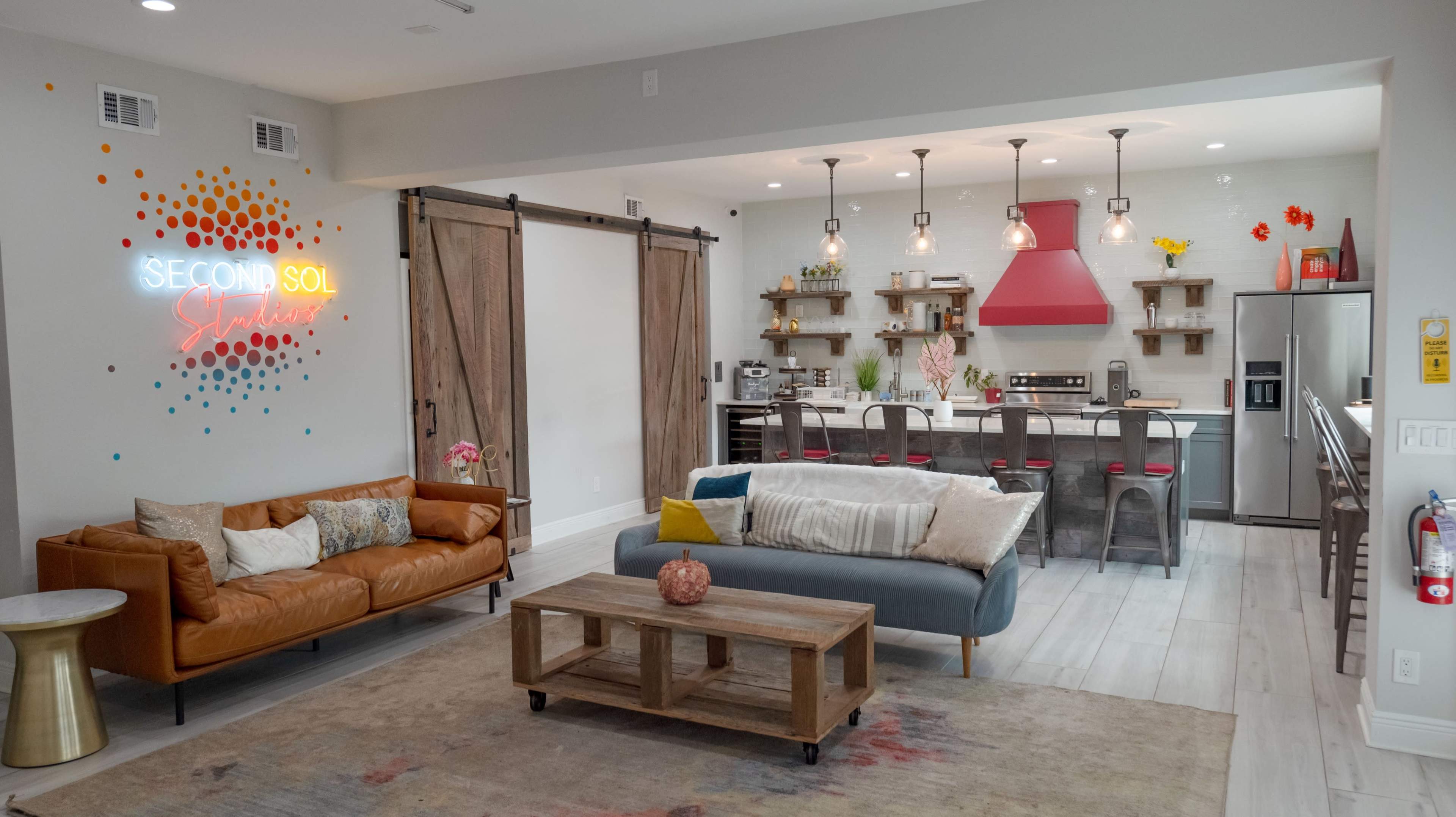 An open-concept living space featuring a leather sofa, a wooden coffee table, and a kitchen with modern appliances and decorative lighting.