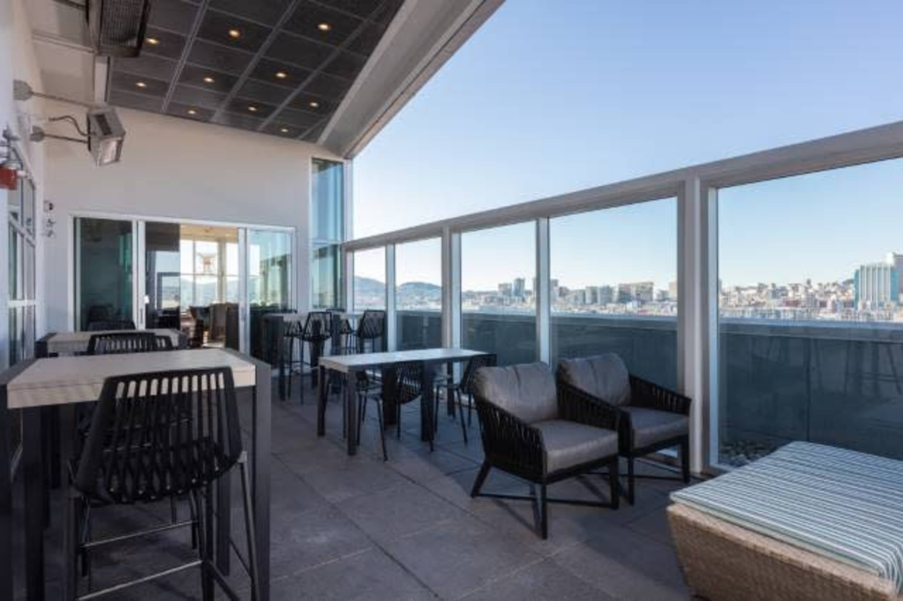 A rooftop terrace features a set of tables and chairs with city skyline views in the background.