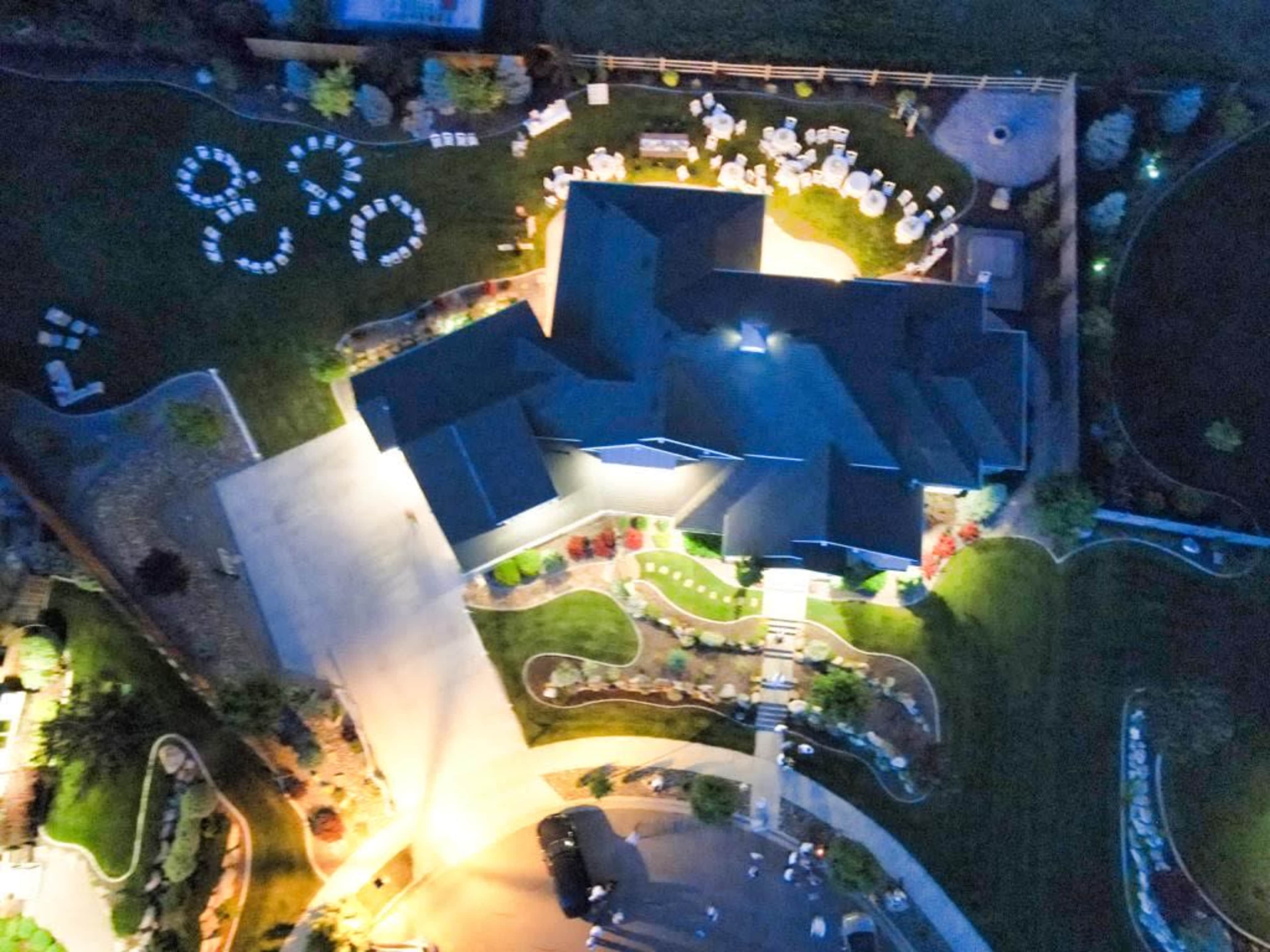 An aerial view shows a large house surrounded by landscaped gardens and seating arranged for an event in the yard.