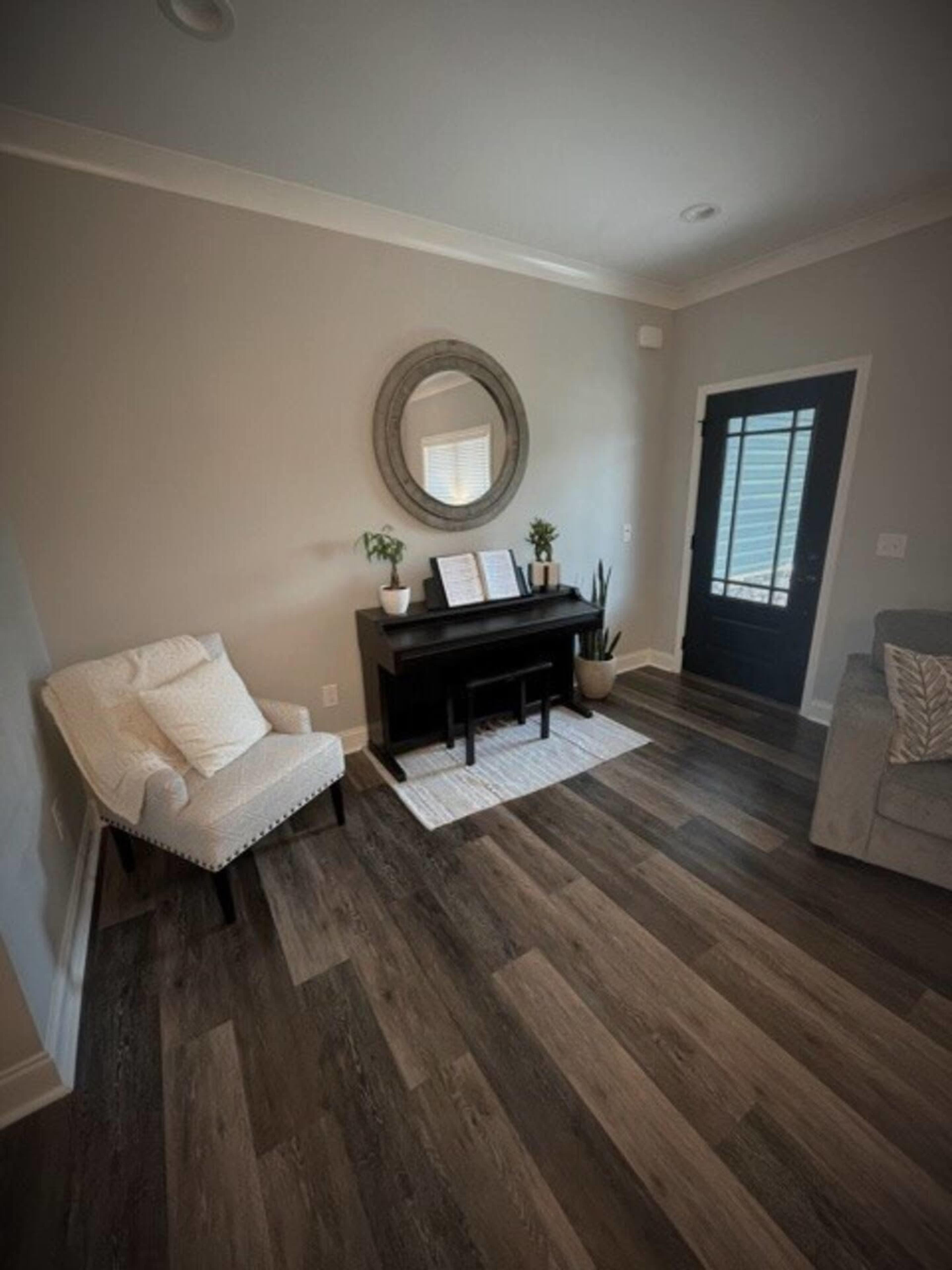 A corner of a living room featuring a black piano, a decorative mirror, a chair, and a door leading outside.