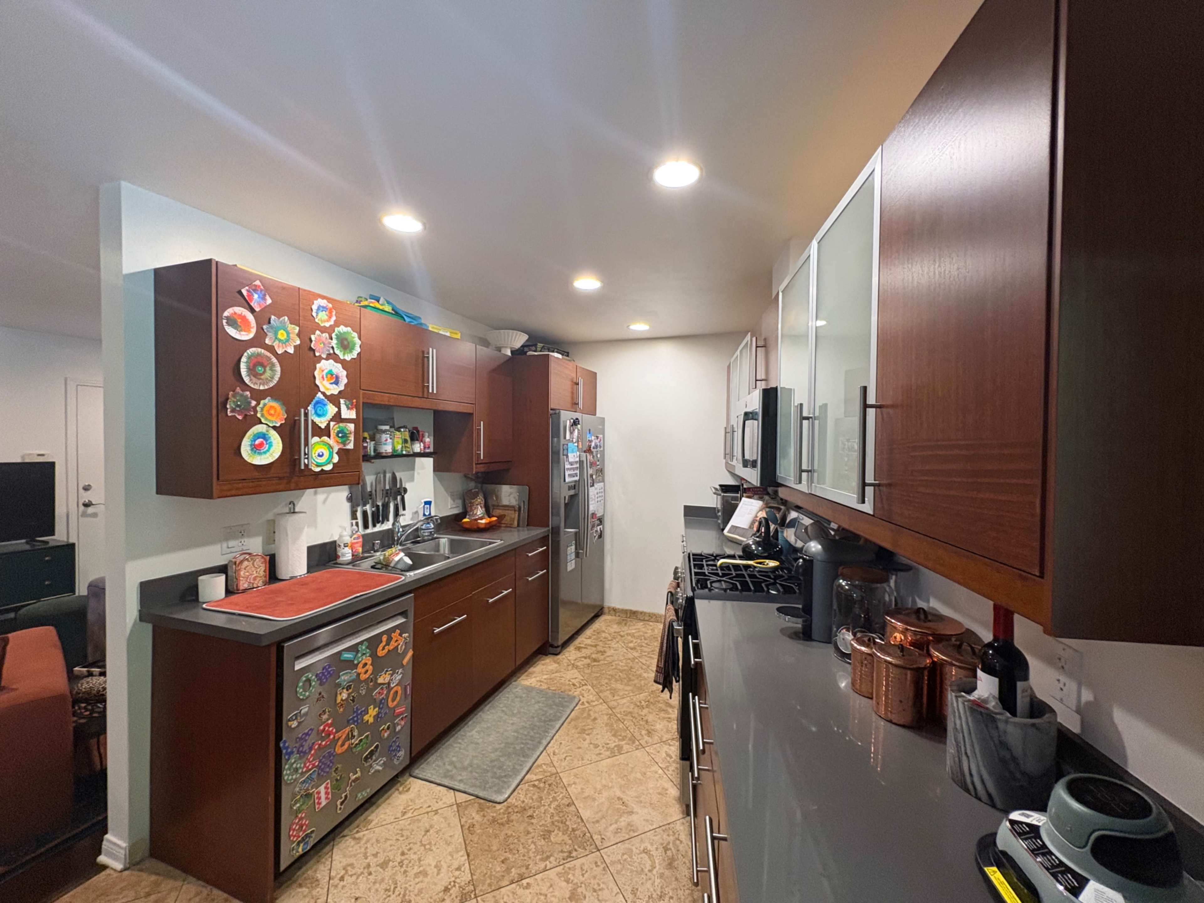 The kitchen features brown cabinetry, stainless steel appliances, and a gray countertop with decorative magnets on the fridge.