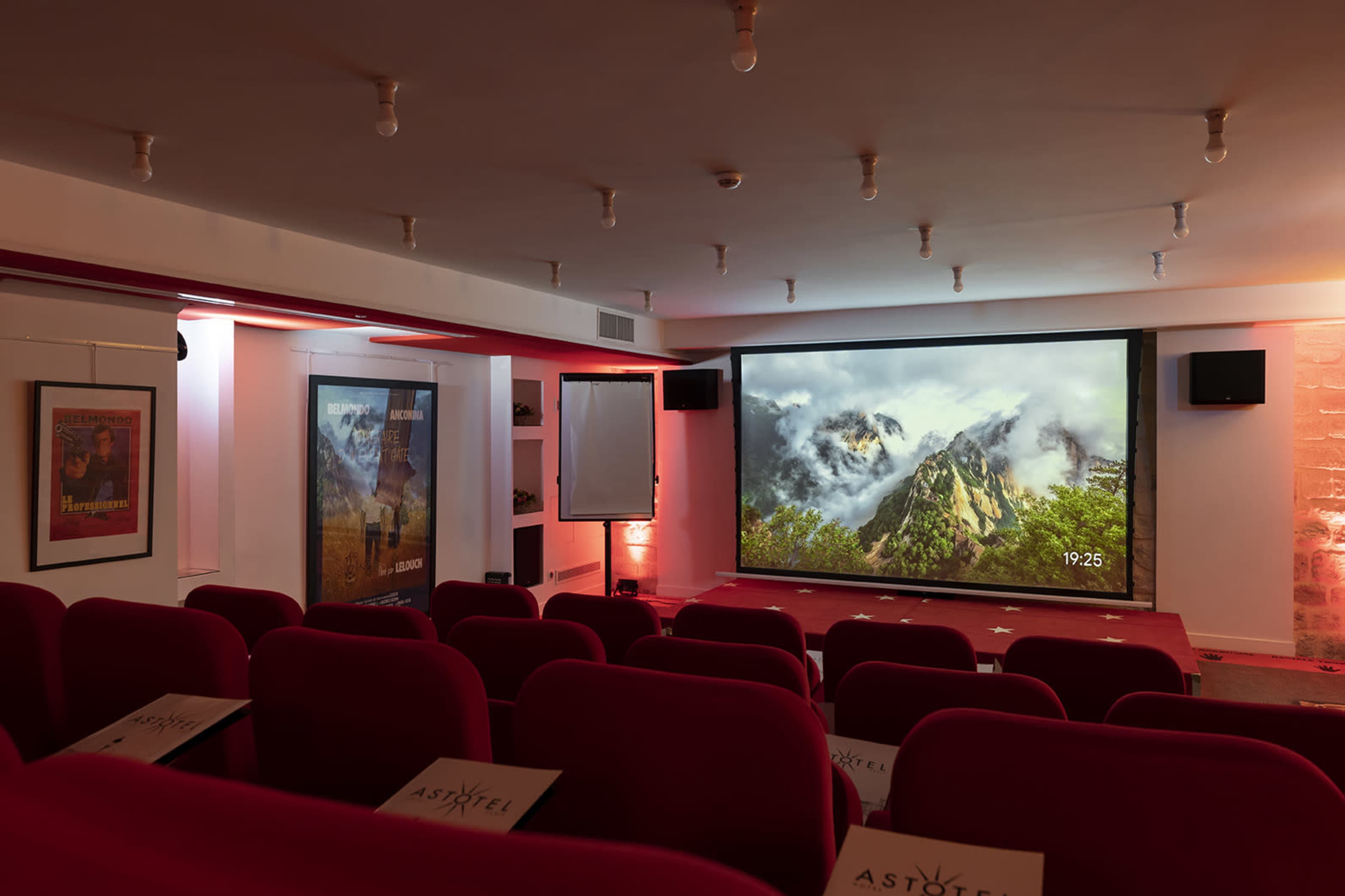 A small theater with red seating and a large screen displaying a mountain scene.