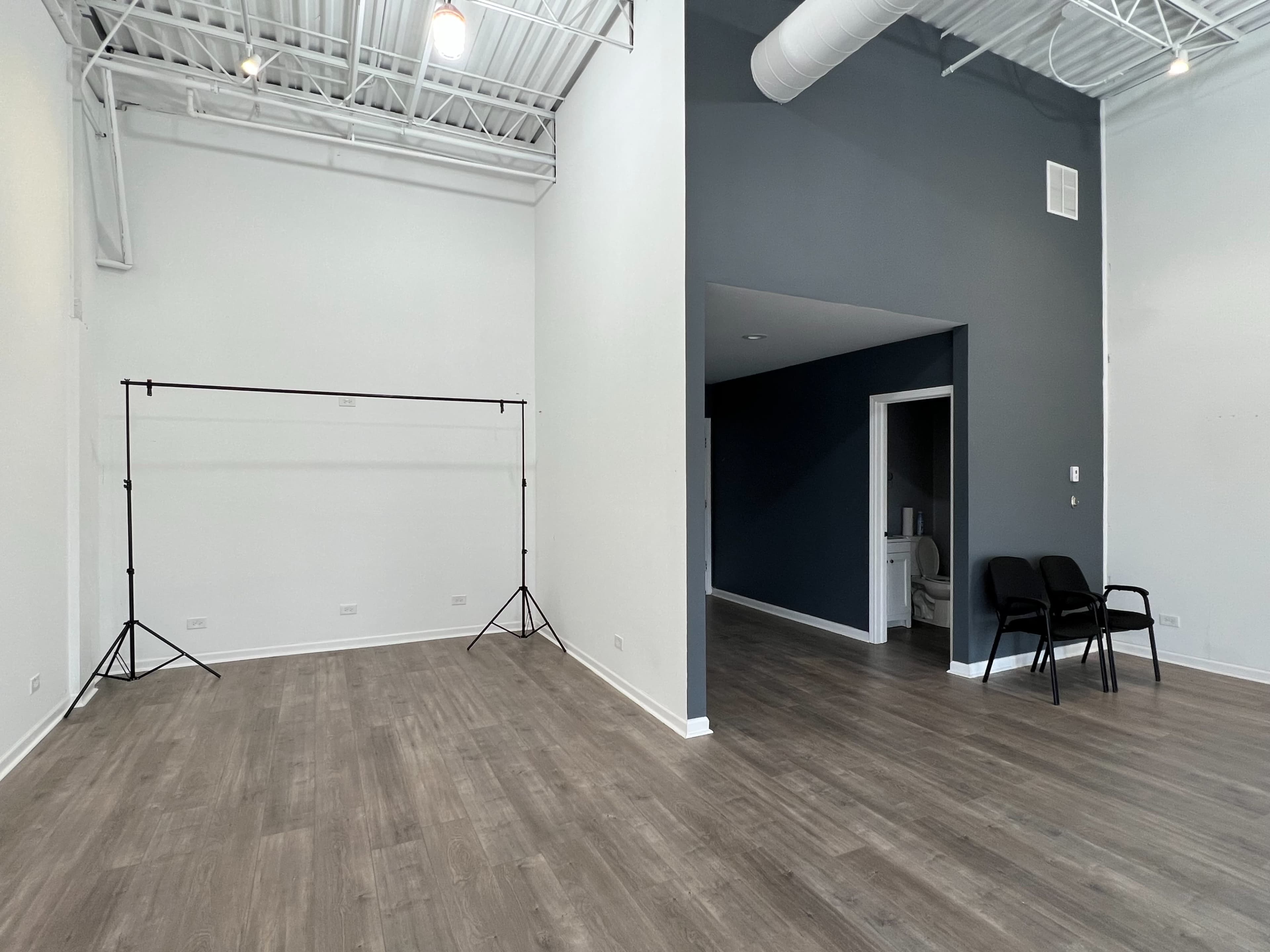 A spacious, minimalistic room with light wood flooring, a dark gray accent wall, and a simple backdrop setup in the corner.